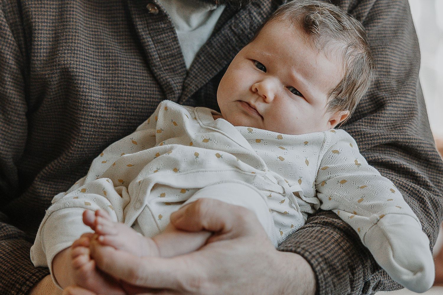 A sleeping baby wearing a white onesie rests peacefully on gray bedding.