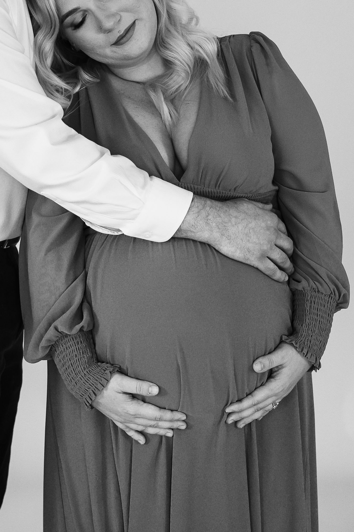 Hands gently caressing a pregnant belly in a gray maternity dress shown in a series of black and white photos.