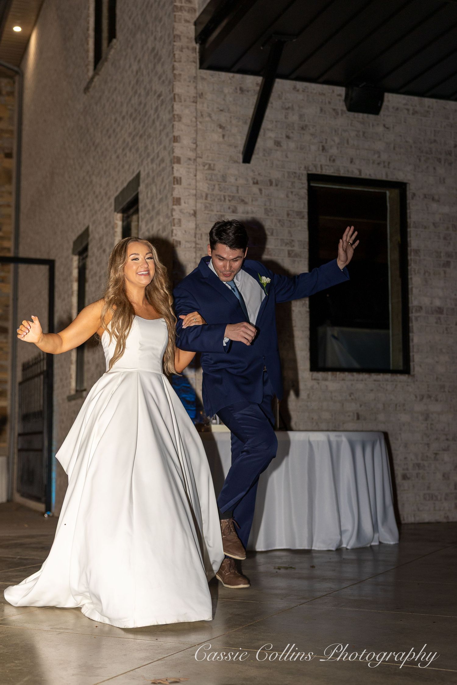 A couple dances together at a wedding reception in a rustic brick-walled venue with white table linens.