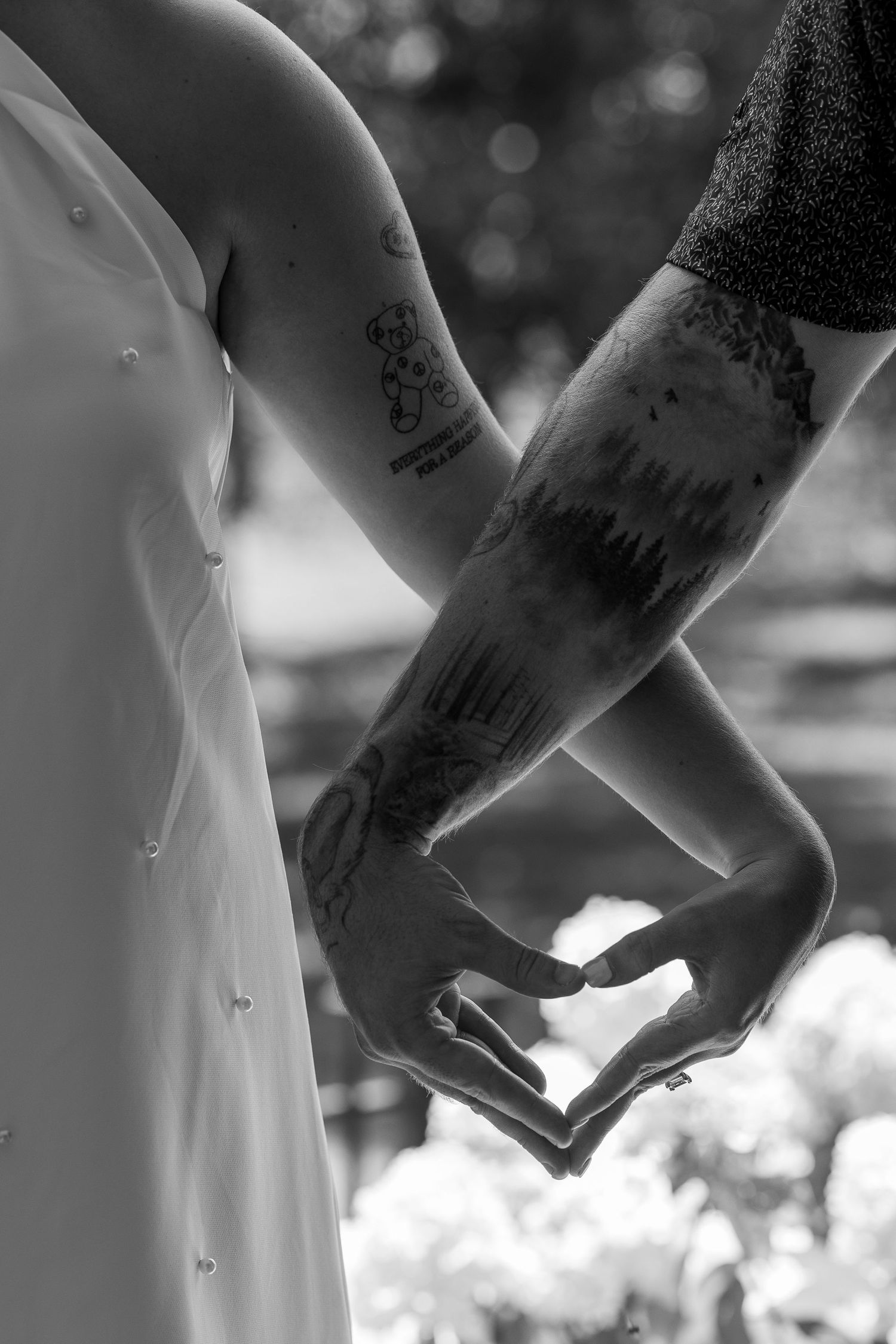 Couple with tattoos forming a heart shape with their hands in a black and white wedding photo.