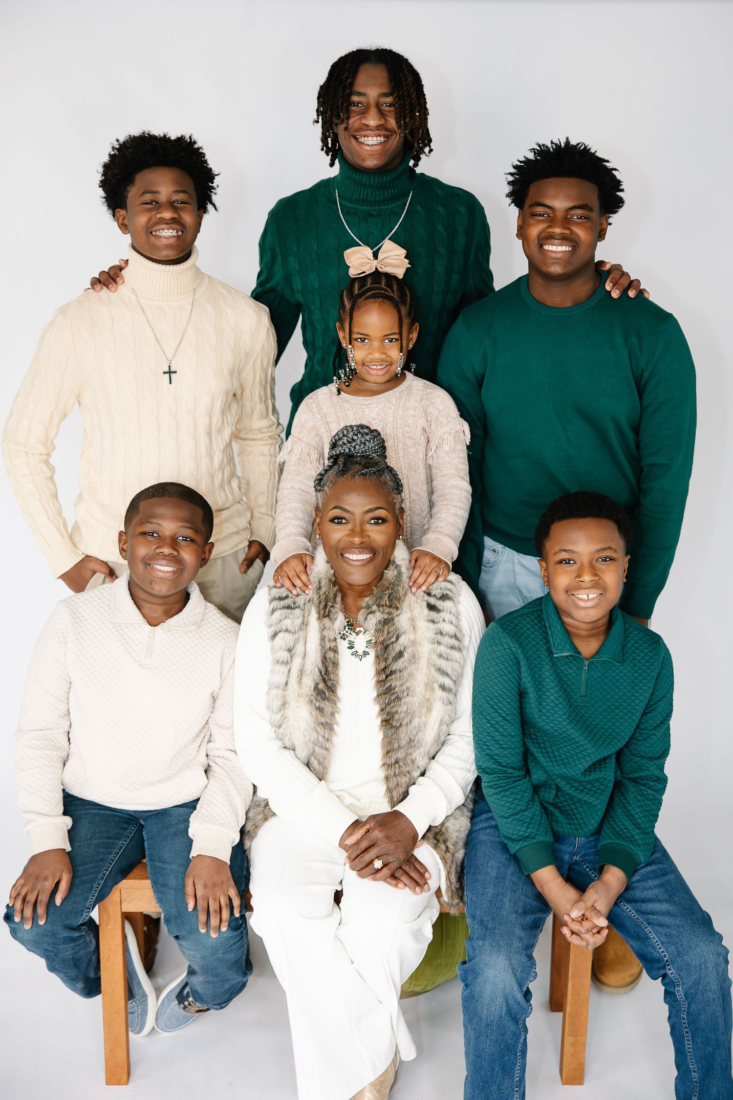 A family portrait with coordinated outfits in green and cream colors against a white background.
