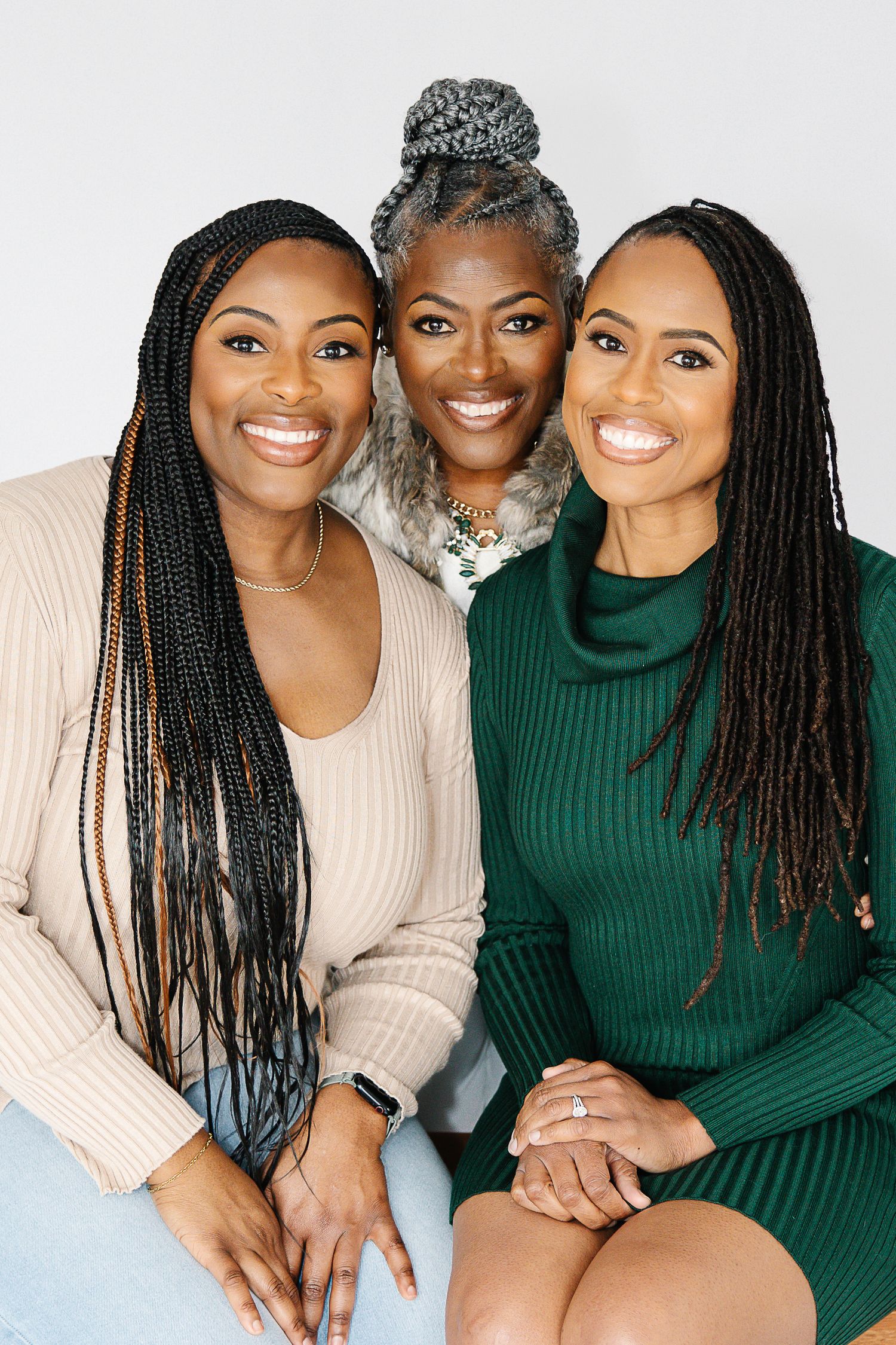 Three people wearing beige and green sweaters pose together for a series of casual studio portraits.