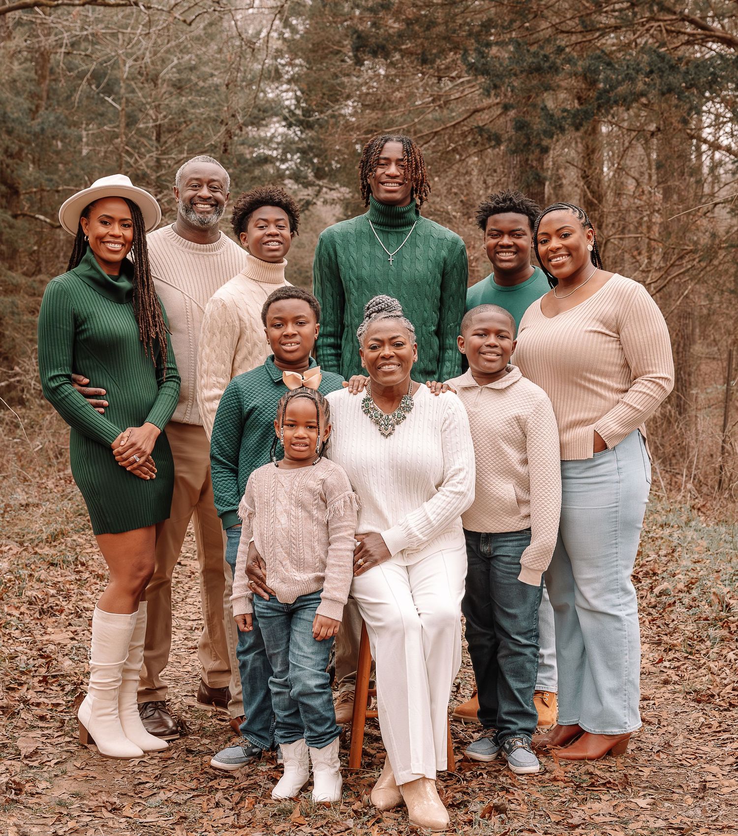 A group in coordinated neutral outfits poses together in an outdoor wooded setting during a family photoshoot.