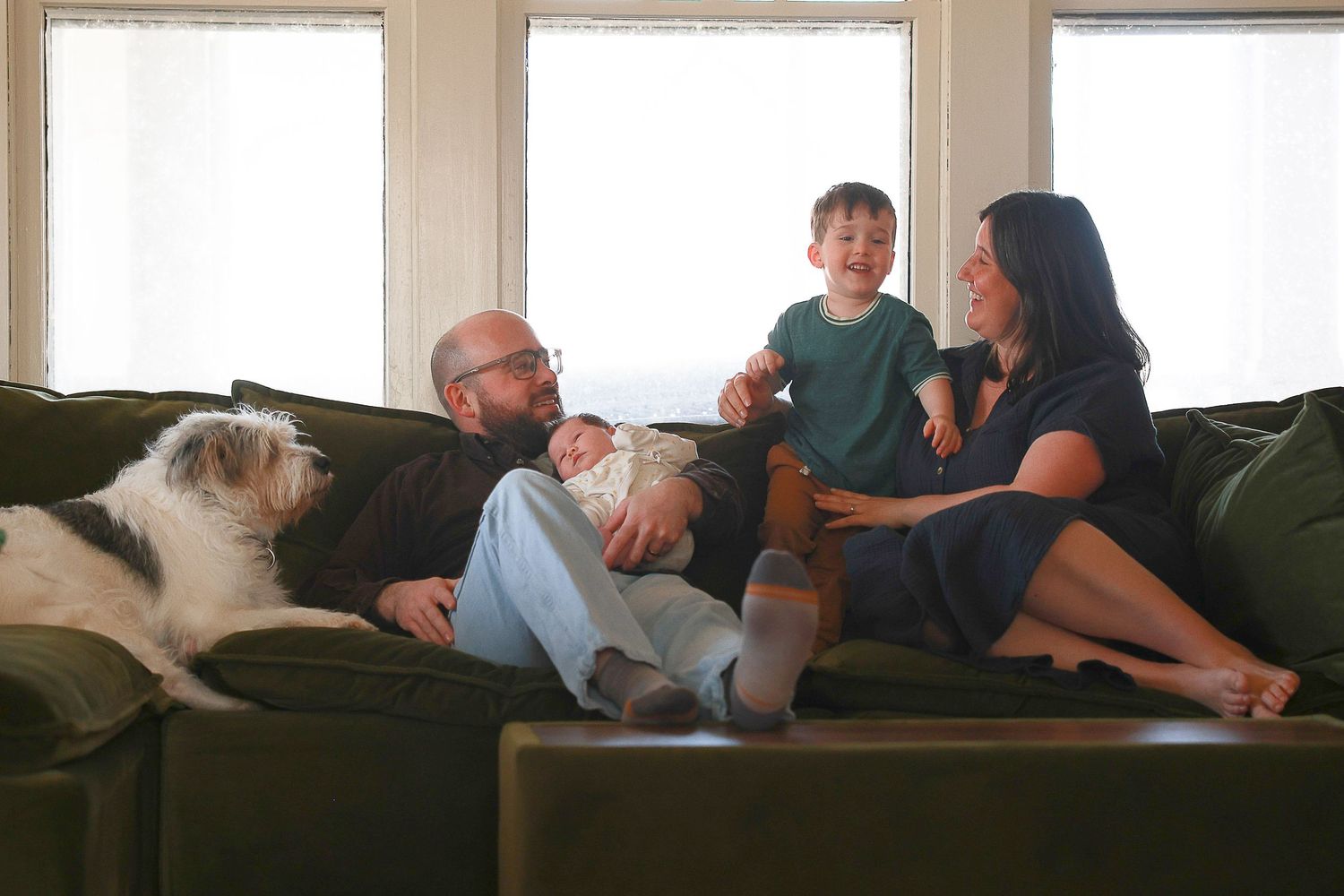 People relaxing together on a couch in a sunlit room with windows in the background.