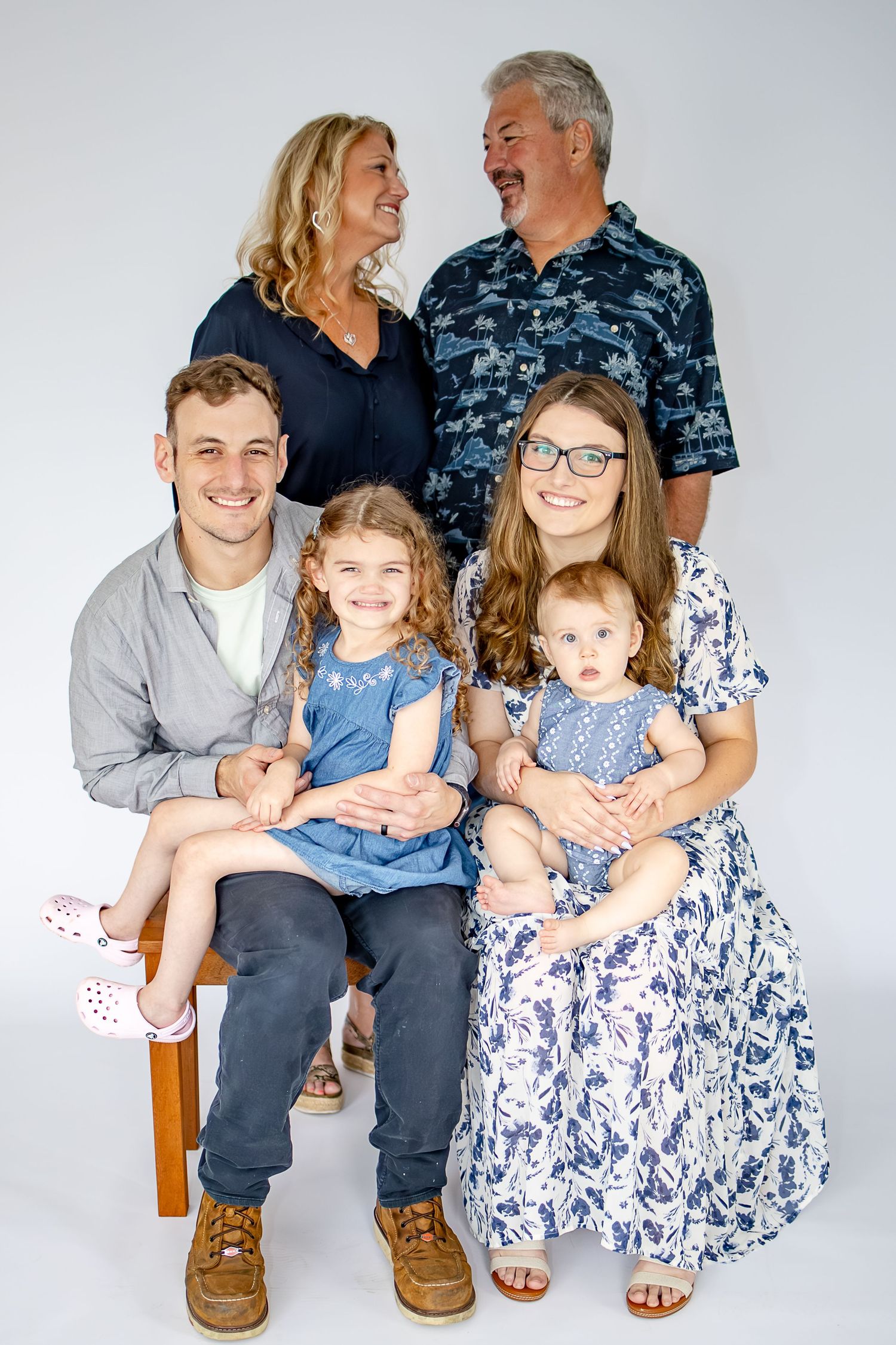 Multi-generational family portrait with grandparents, parents, and two young girls dressed in coordinating blue outfits.
