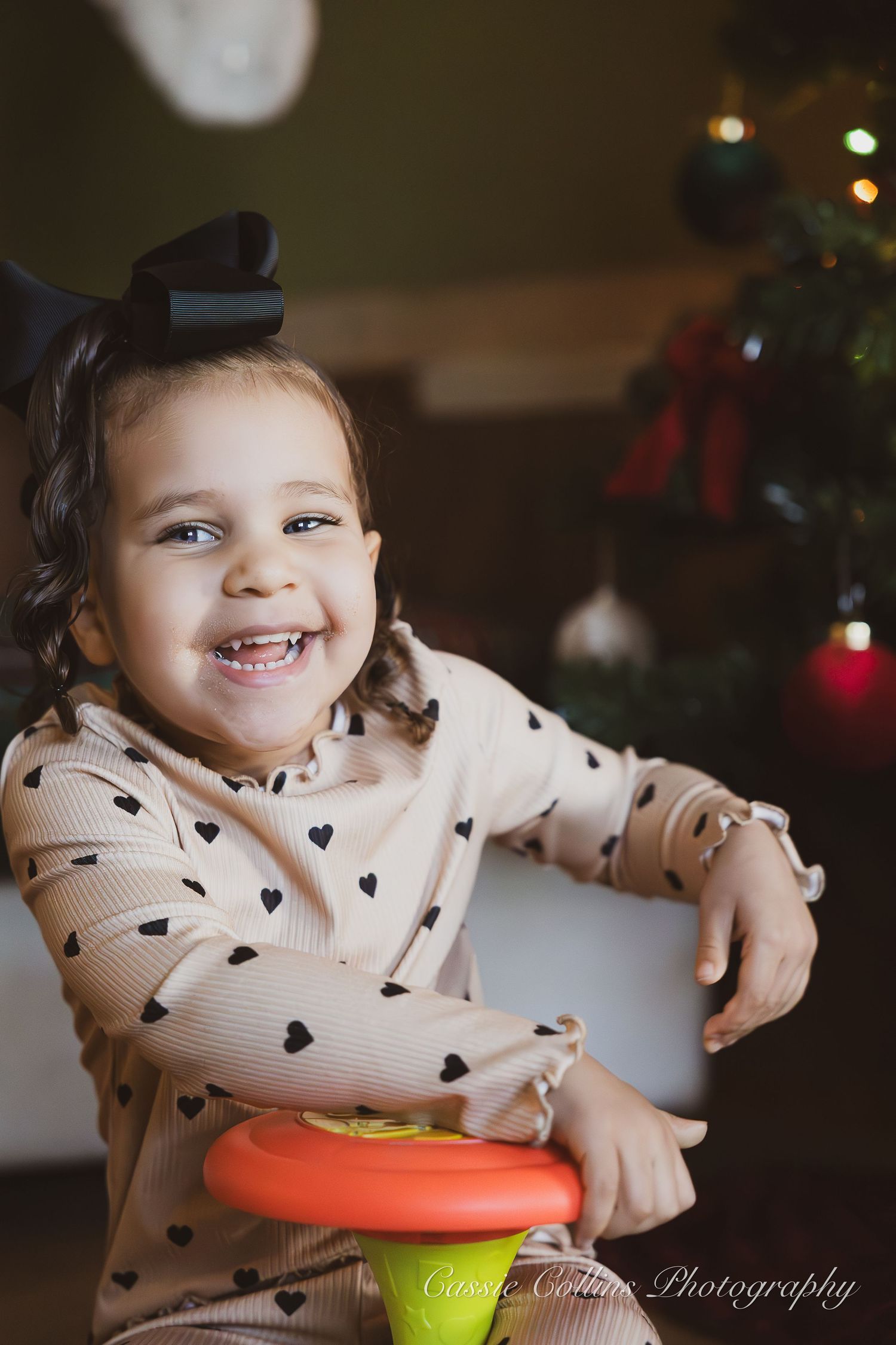 A series of photos showing a child in a heart-patterned sweater playing with a colorful toy during the holidays.
