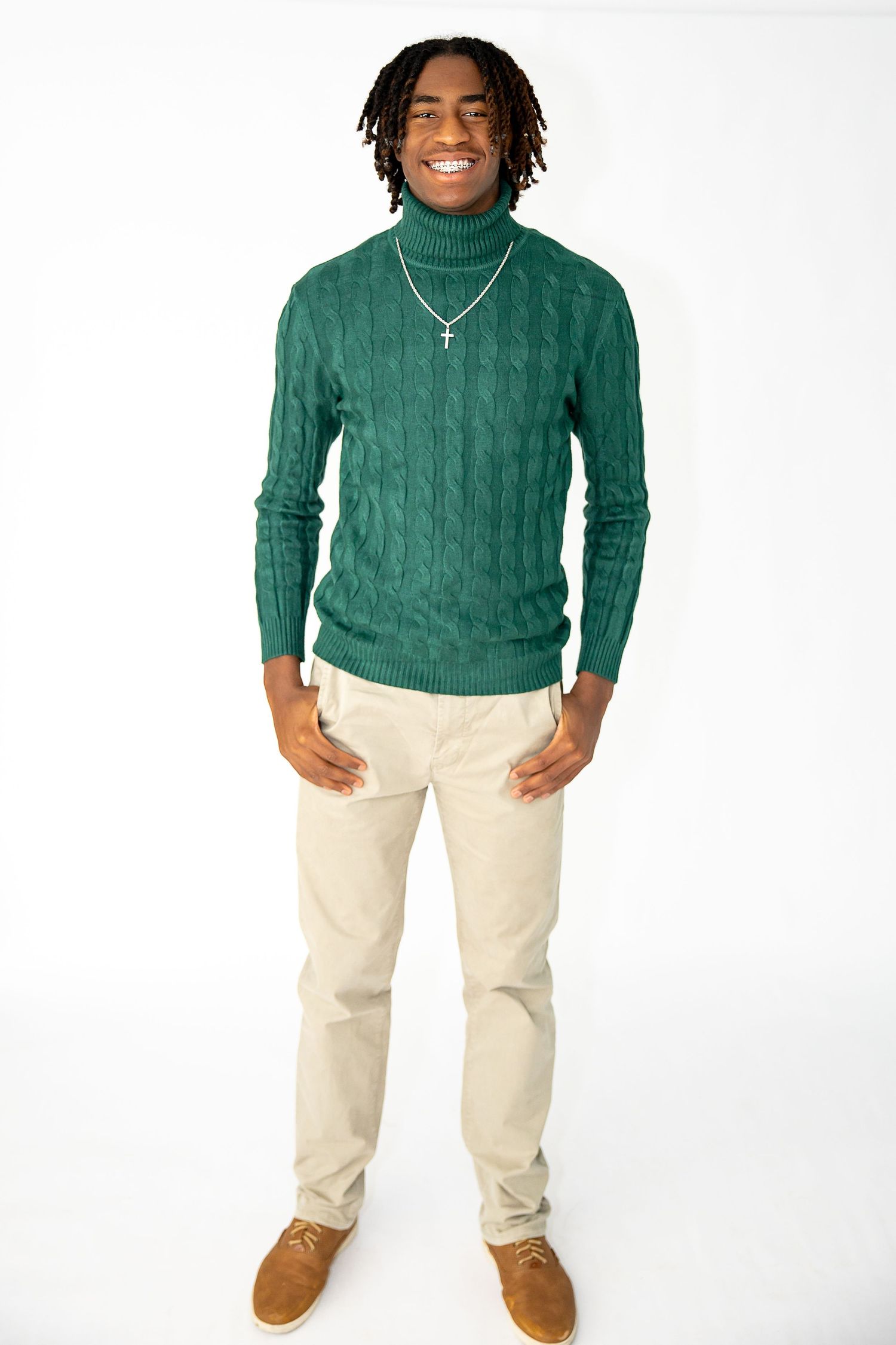Person wearing a green cable knit turtleneck sweater and khaki pants poses against a white background.