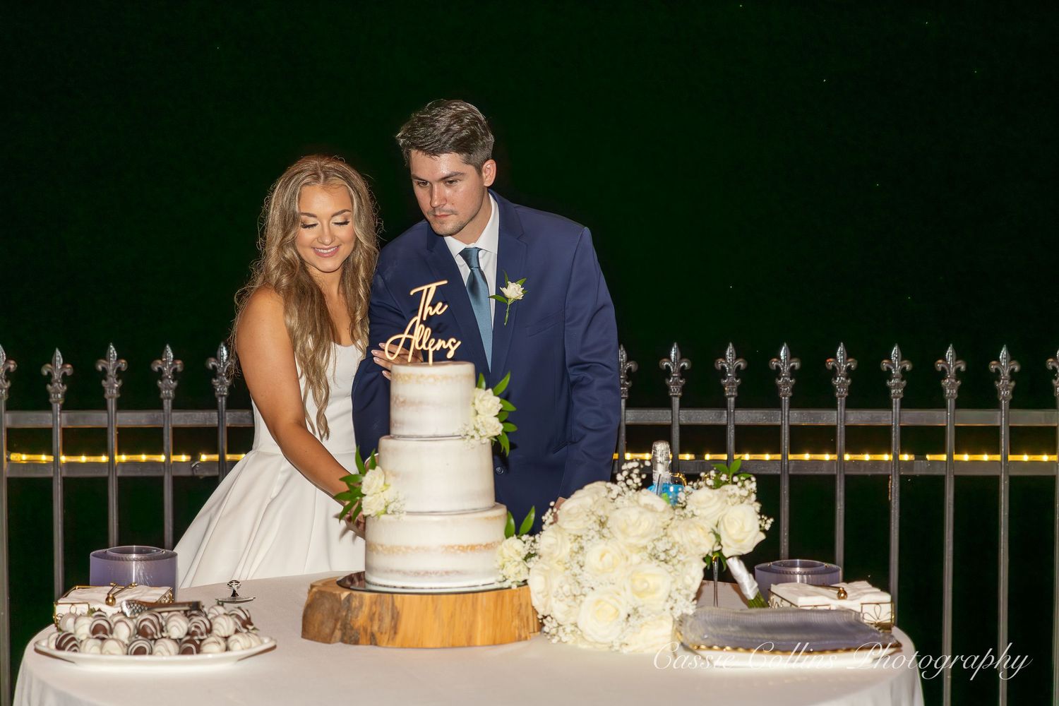 A couple in wedding attire cut their rustic wedding cake together at an outdoor reception.