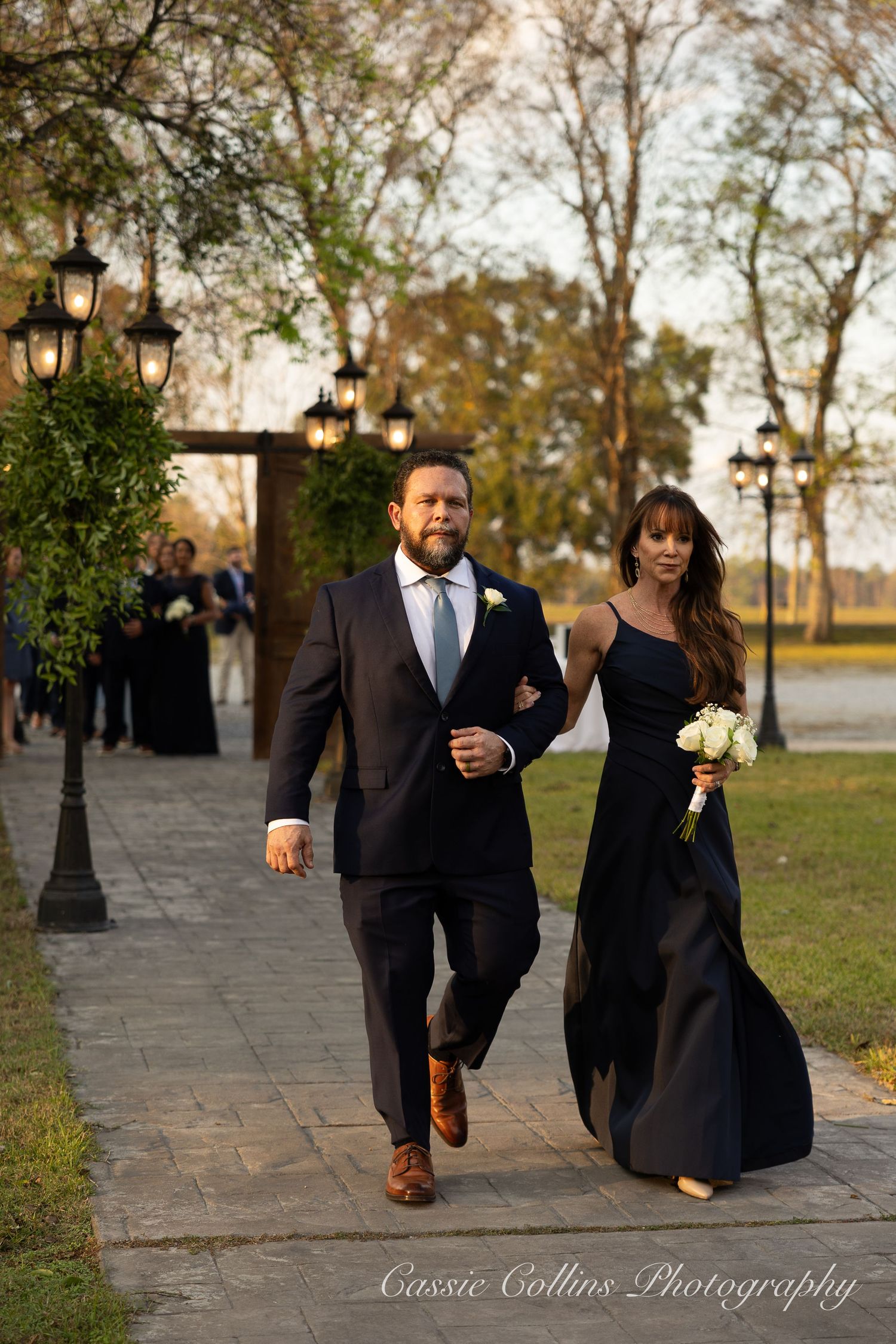 Sequence of black and white photos showing a couple walking along a stone pathway at sunset with lamp posts nearby.