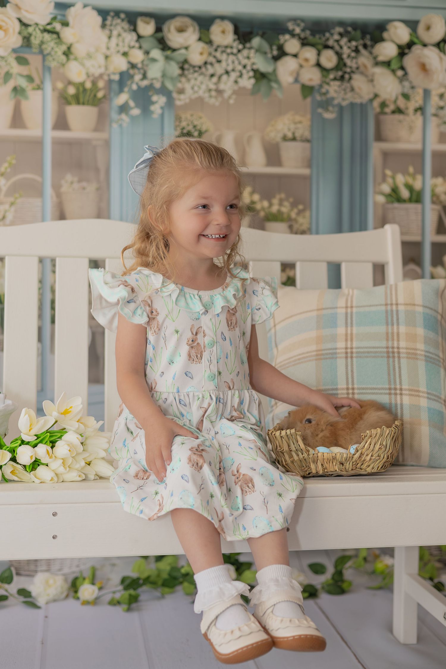 A child in a floral dress sits on a white bench surrounded by delicate white flowers and decorative elements.