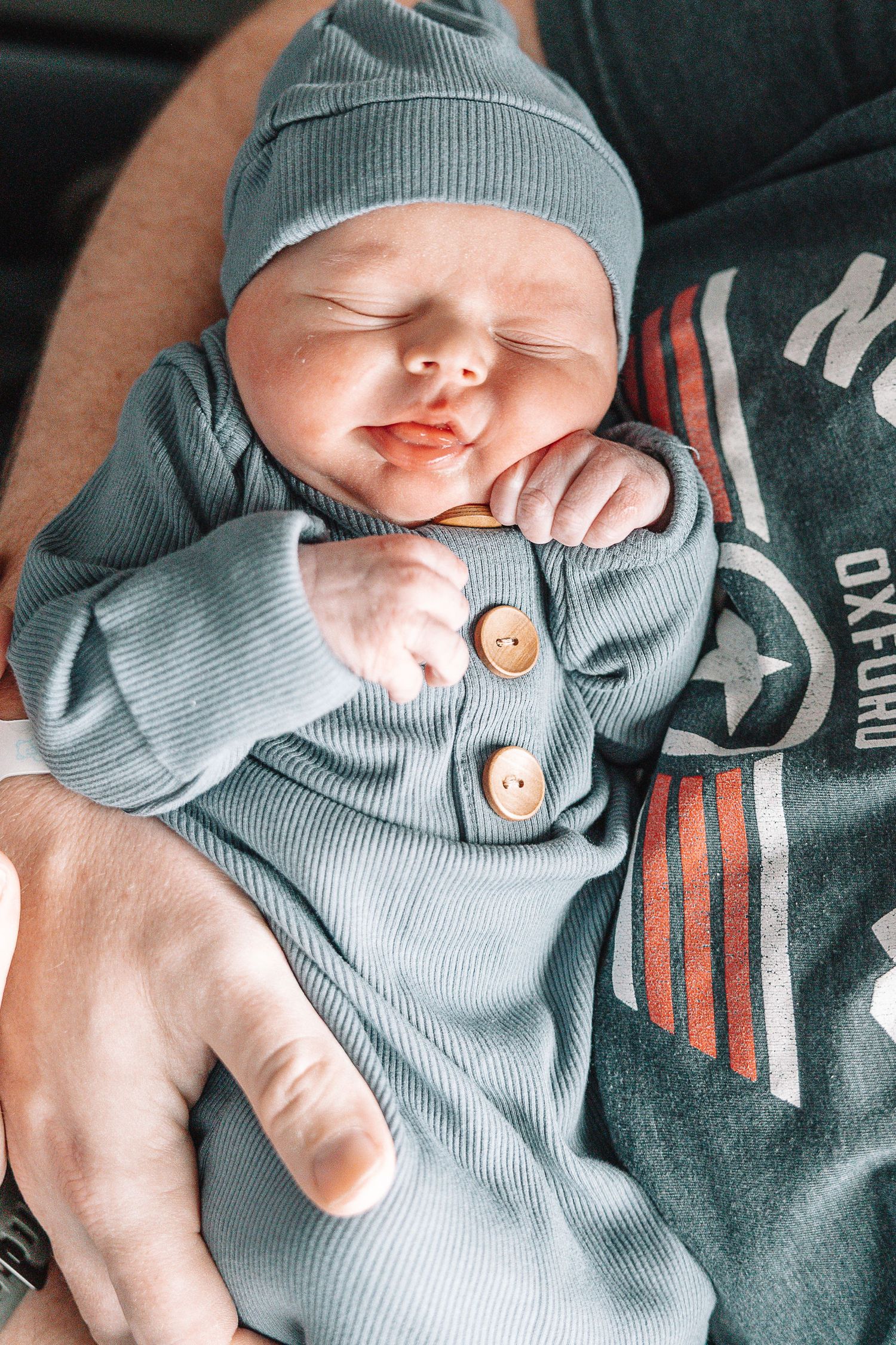 Newborn baby wearing a soft gray outfit with decorative buttons lies peacefully in a series of close-up shots.