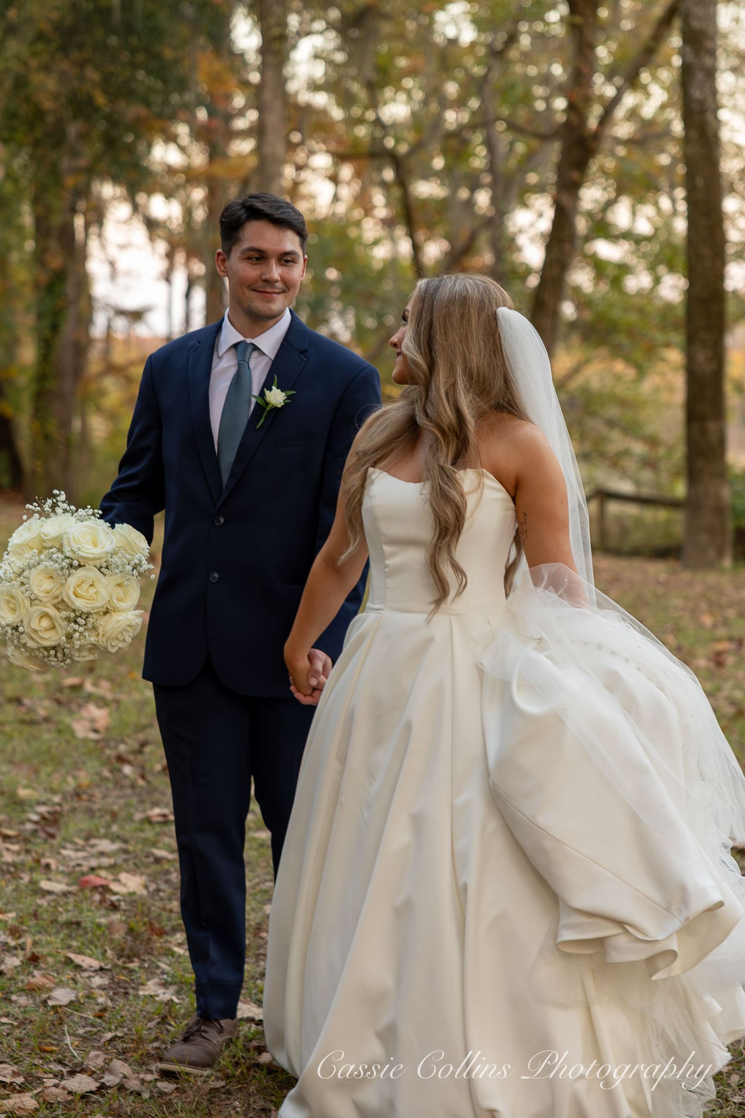 A couple shares a joyful moment in their wedding attire among autumn trees during an outdoor photo session.