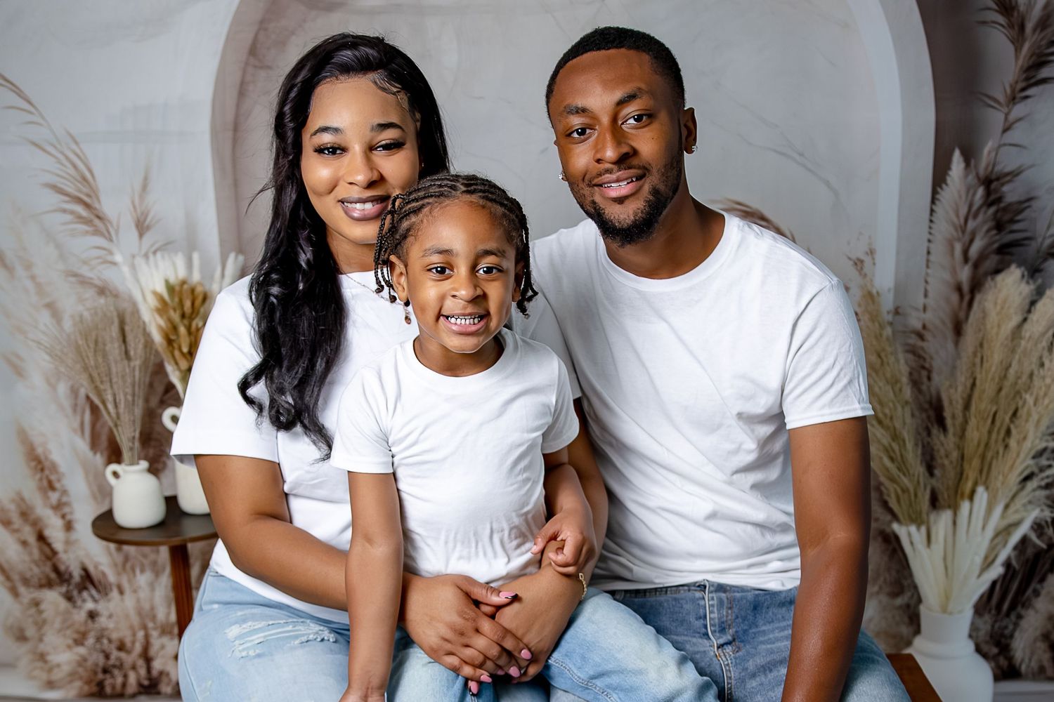 A happy family of three wearing white shirts and jeans posing together for a portrait photo.