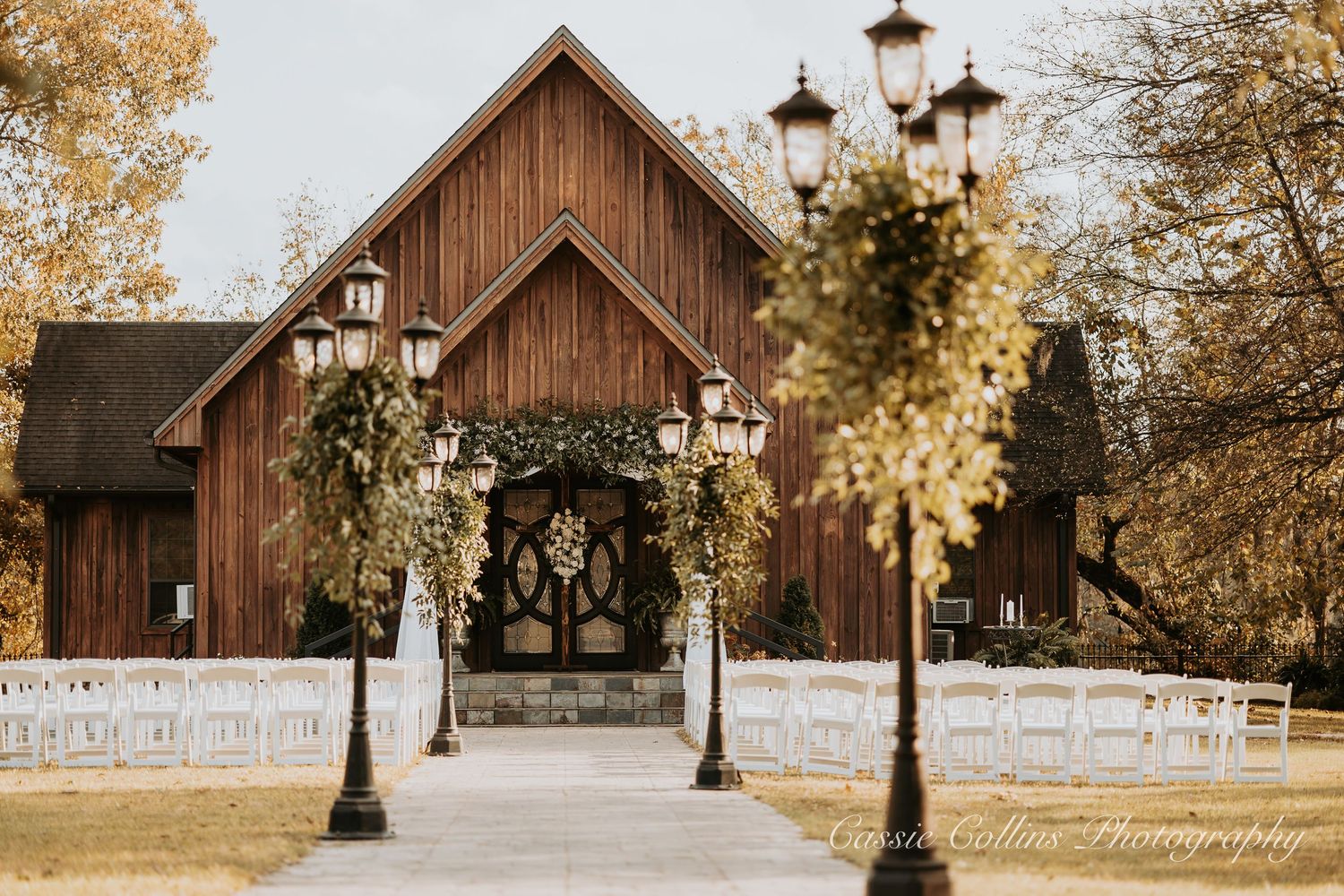 Rustic wooden barn wedding venue with vintage lamp posts and autumn trees in golden afternoon light.