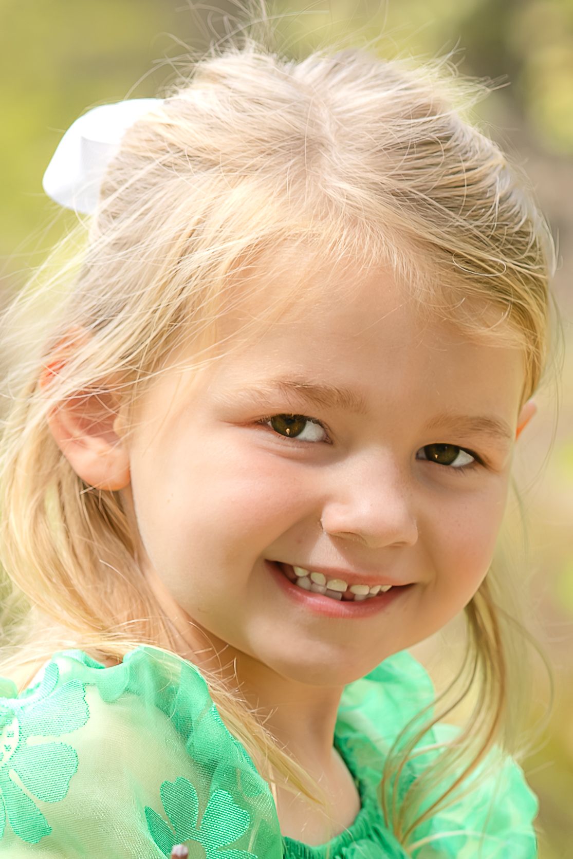A series of four photos showing a young child in a green dress smiling and posing with natural lighting outdoors.