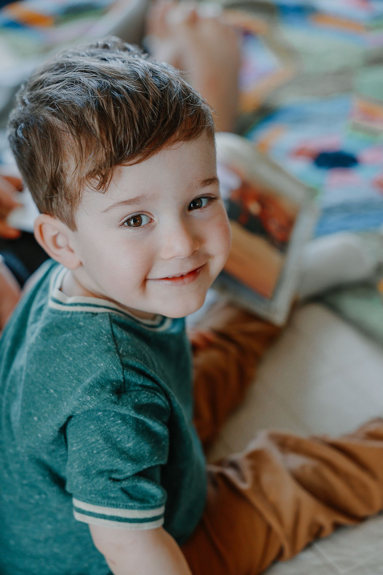 A child wearing a green shirt smiles while lying down on a colorful patterned surface.