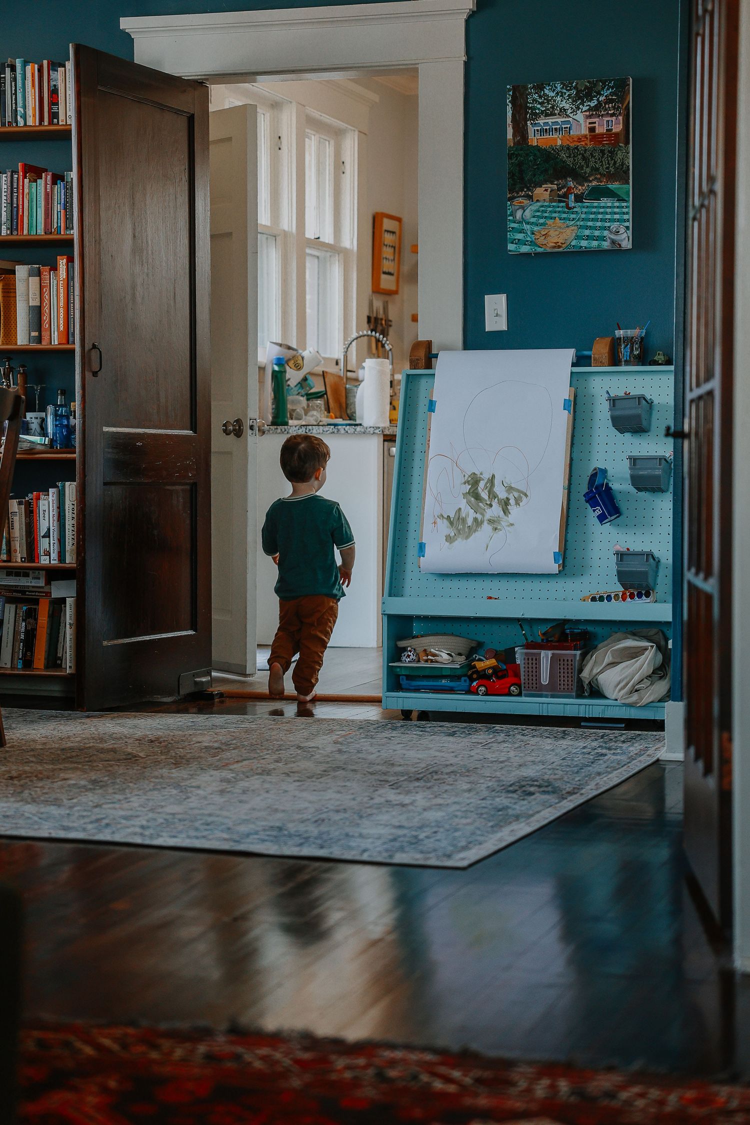 A panoramic view of a cozy home interior with teal walls, bookshelves, and a carpeted floor in natural lighting.