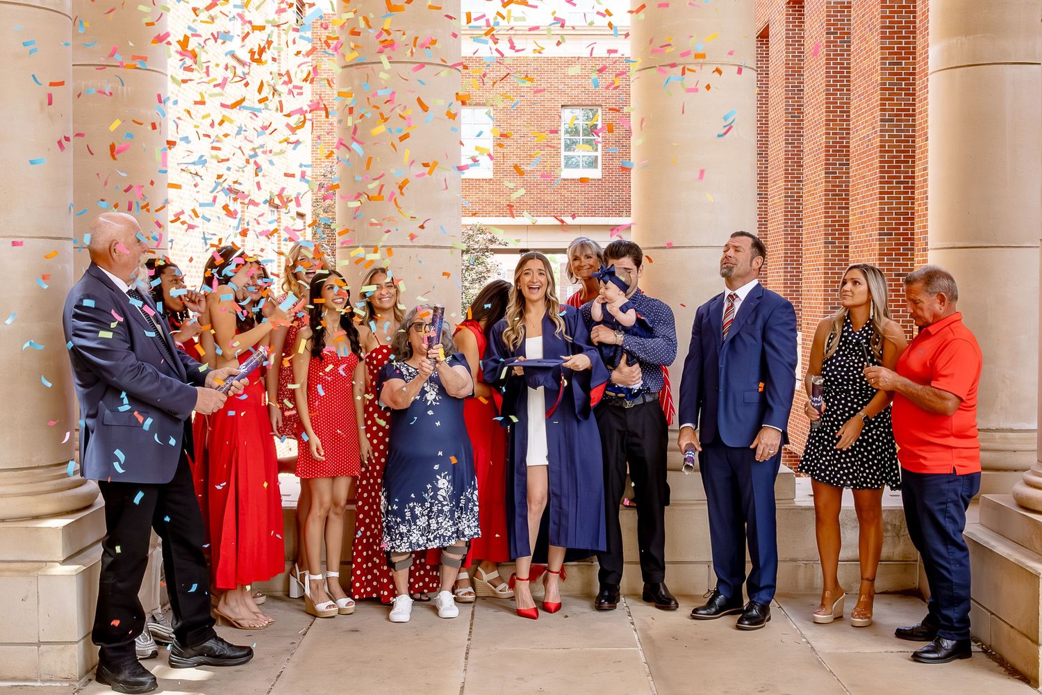 Group of people celebrating with colorful confetti at a wedding ceremony outside a brick building.