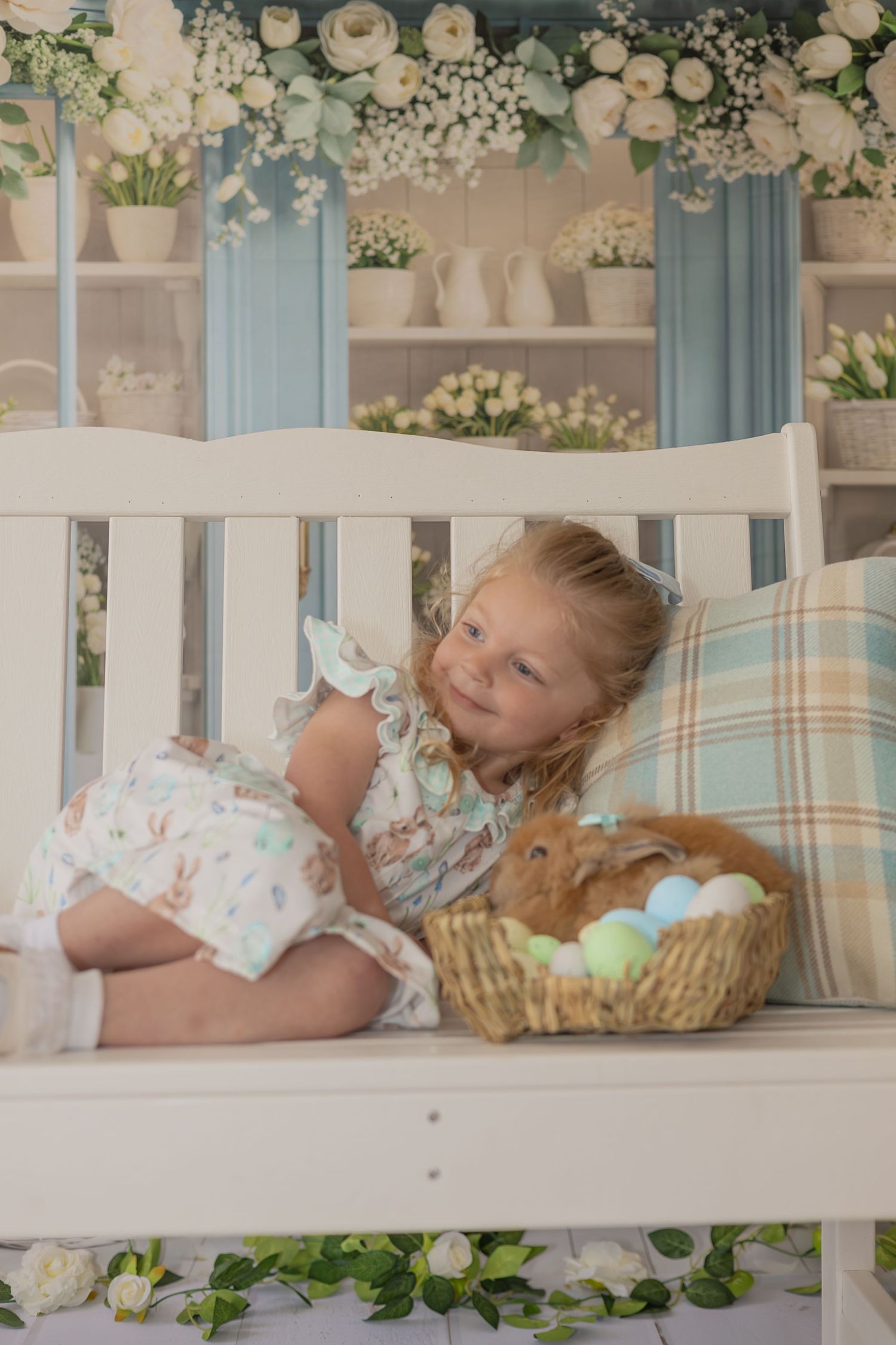 A sleeping child lies on a couch with floral decorations and plush toys in a dreamy nursery setting.