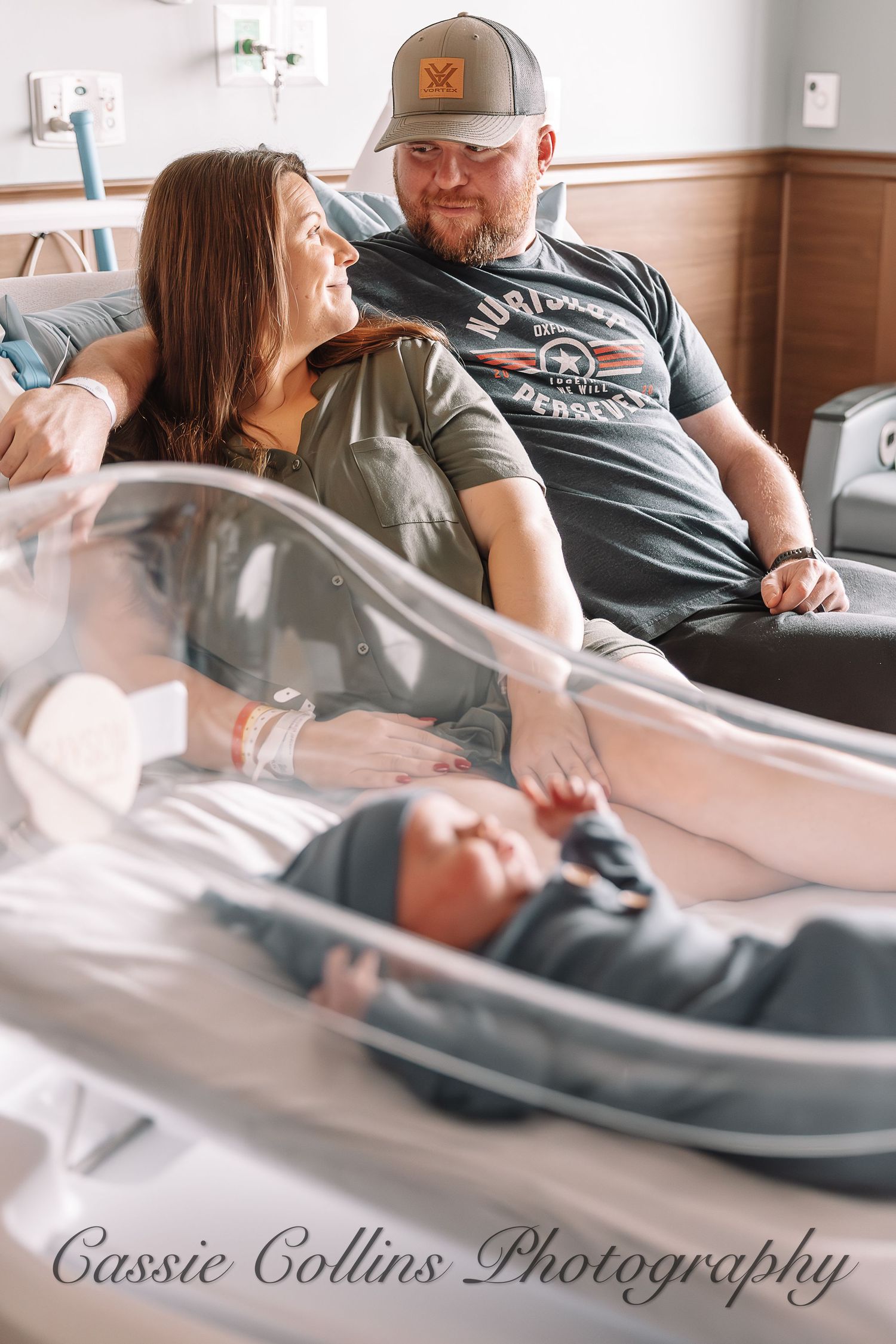 Hospital room scene showing tender moments with a newborn baby in a bassinet while family gathers around.