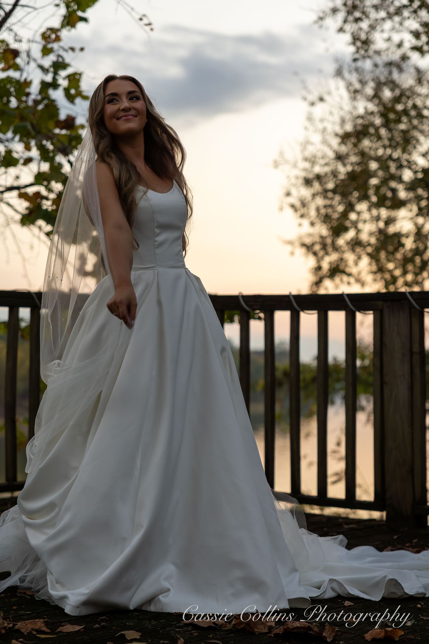 A bridal photoshoot at sunset features flowing white wedding gowns against a rustic wooden railing backdrop.
