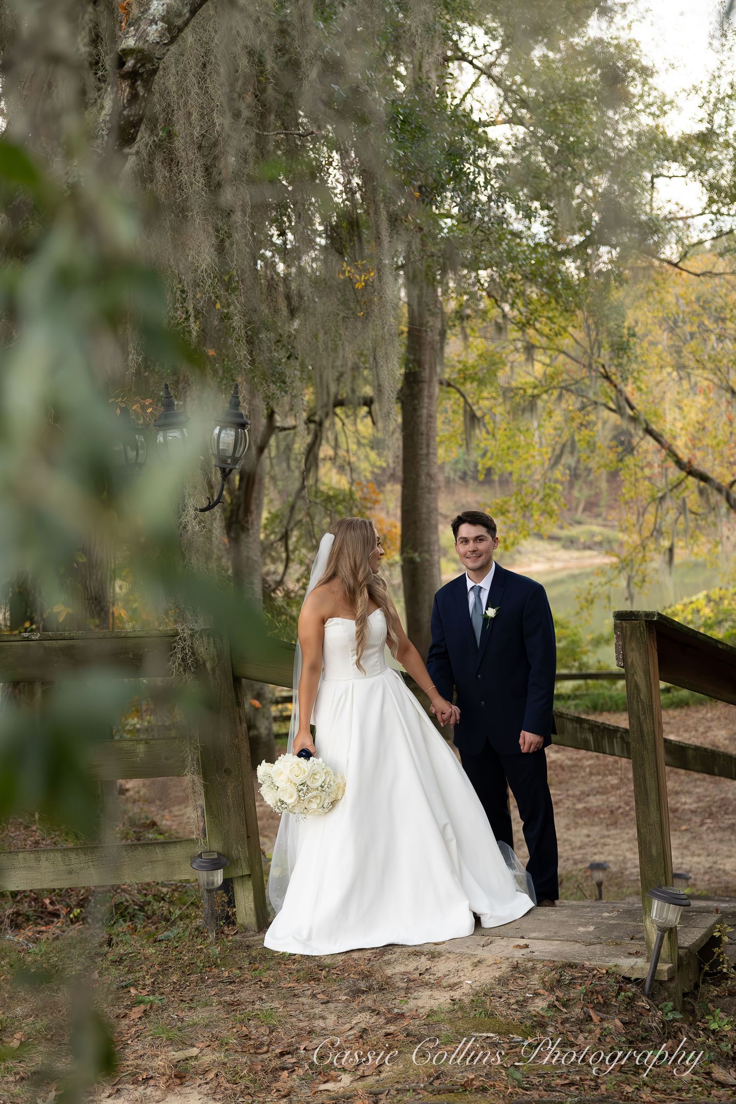 Romantic wedding couple poses together in a wooded outdoor setting with Spanish moss hanging from trees.