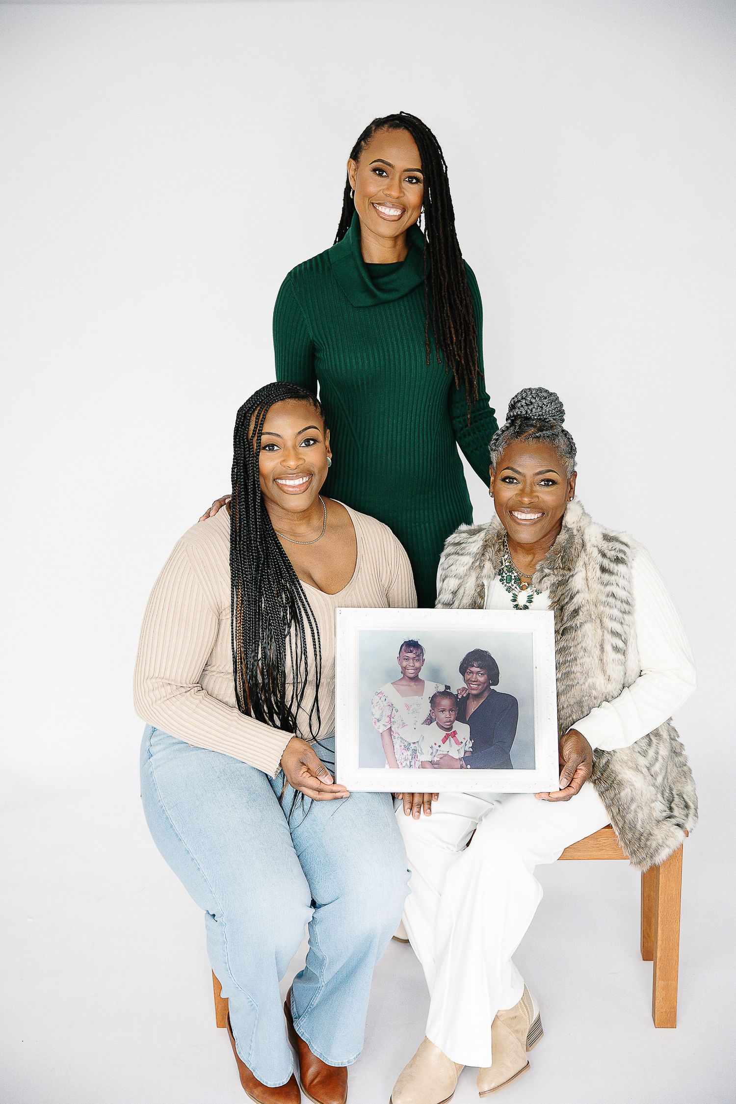 Two people in coordinated outfits pose together while holding a framed photograph during a studio photoshoot.