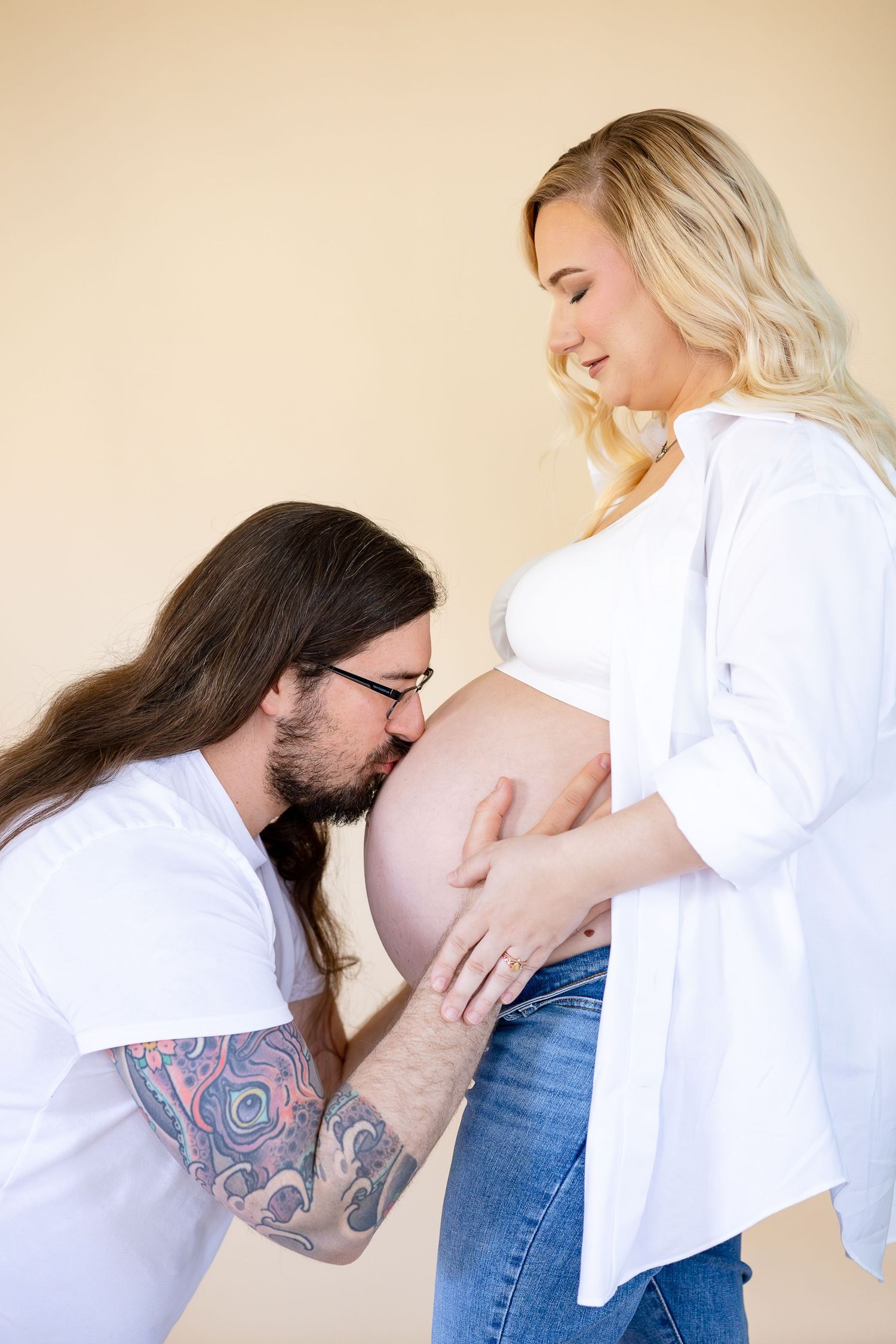 A series of intimate maternity photos showing a person kissing a pregnant belly while wearing a white shirt and jeans.