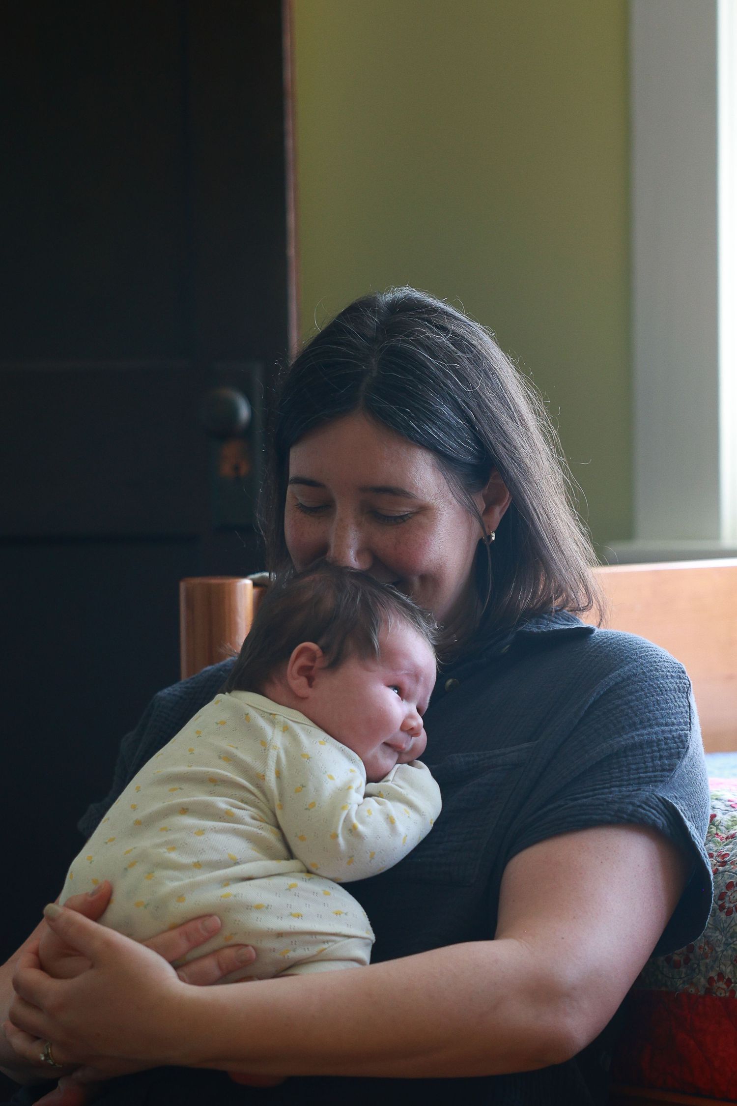 A tender moment captured as a sleeping baby rests peacefully against a caregiver in a dimly lit room.