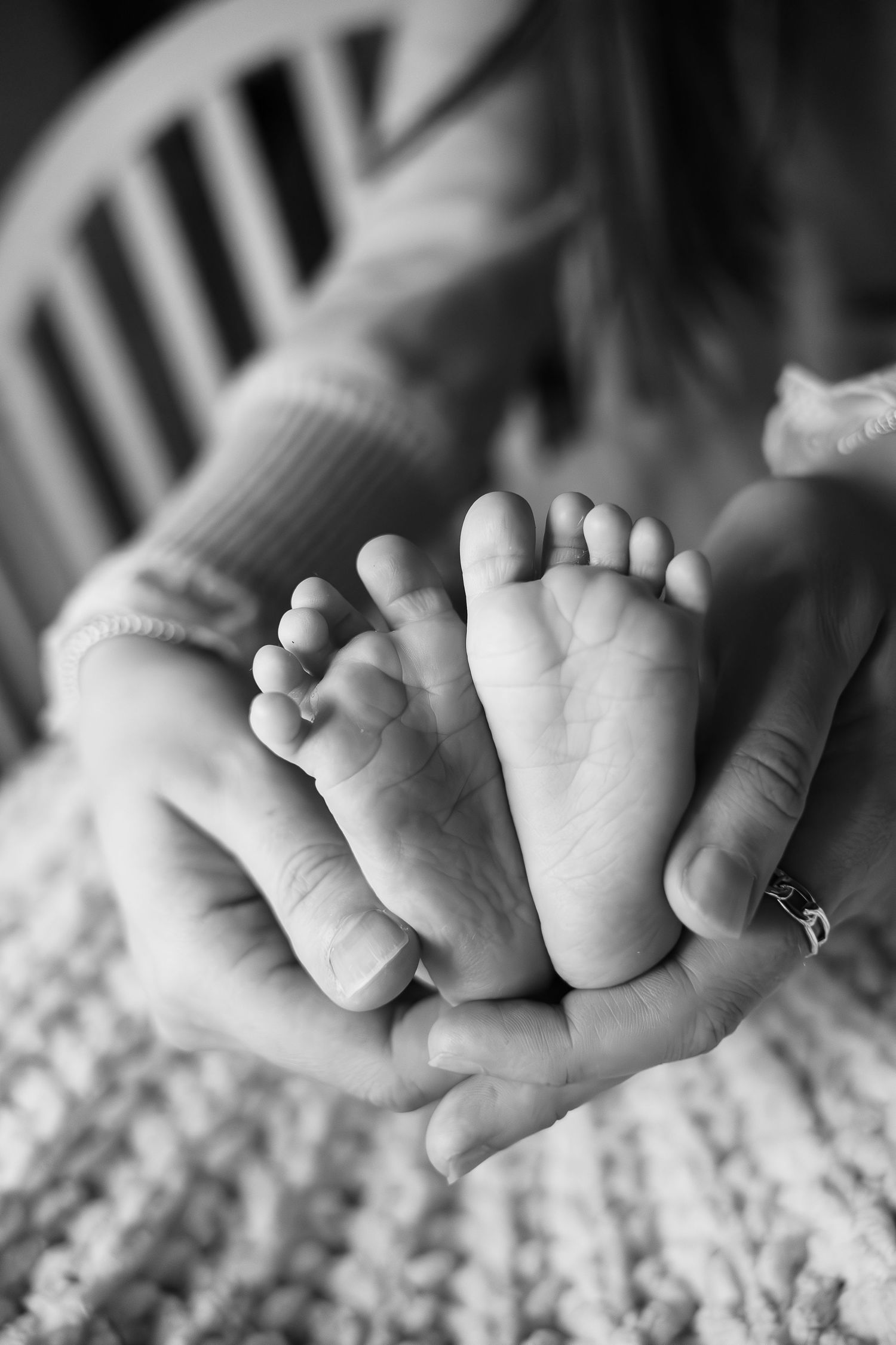 Close-up black and white photograph of tiny newborn baby feet resting on textured blanket.
