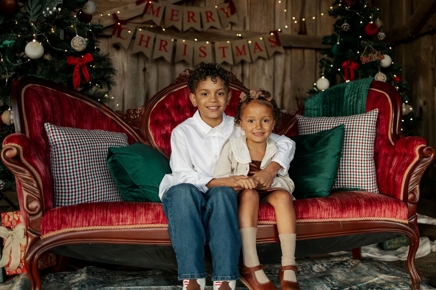 Festive Christmas scene with red velvet vintage couch, decorative pillows, twinkle lights and holiday decor in background.