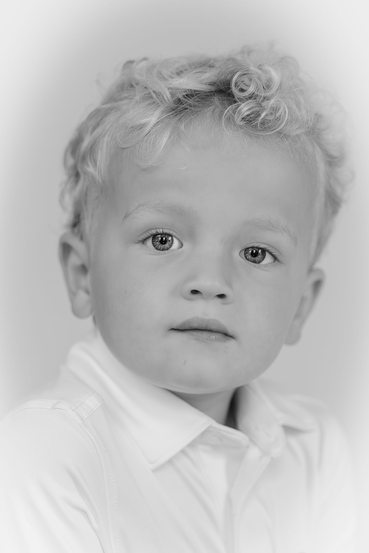 Black and white portrait of a young boy with curly blonde hair wearing a white shirt with suspenders.
