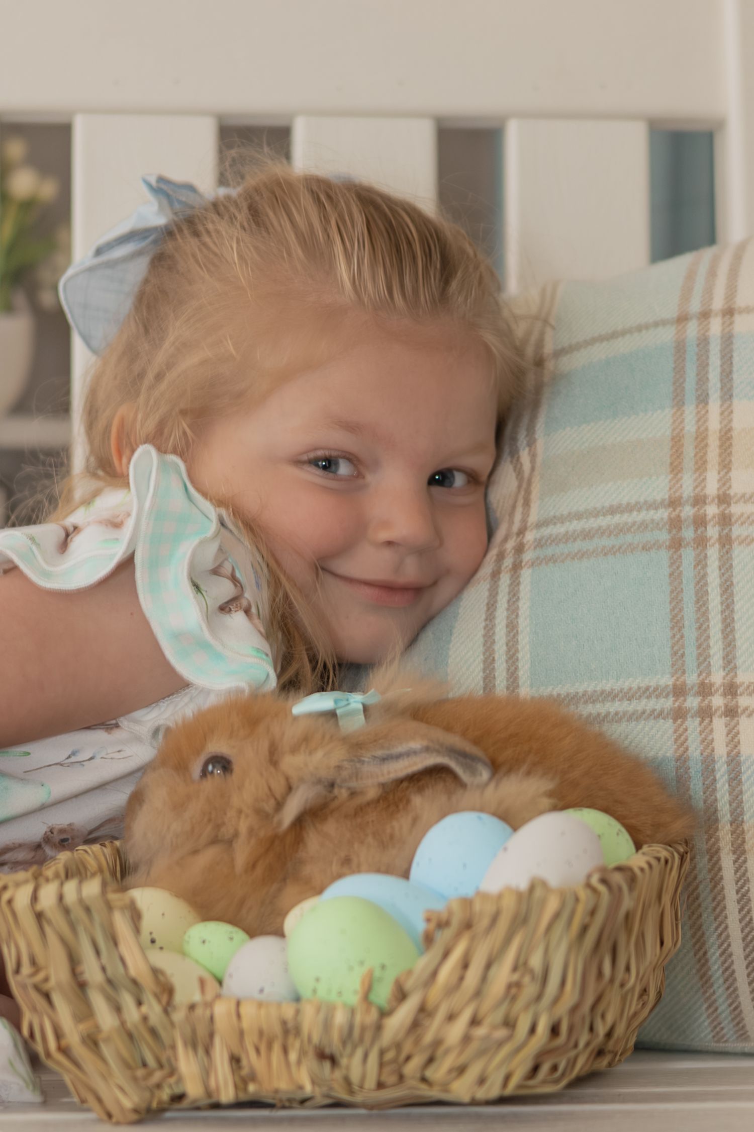A child peeks playfully over the edge of a woven basket filled with pastel-colored Easter eggs.