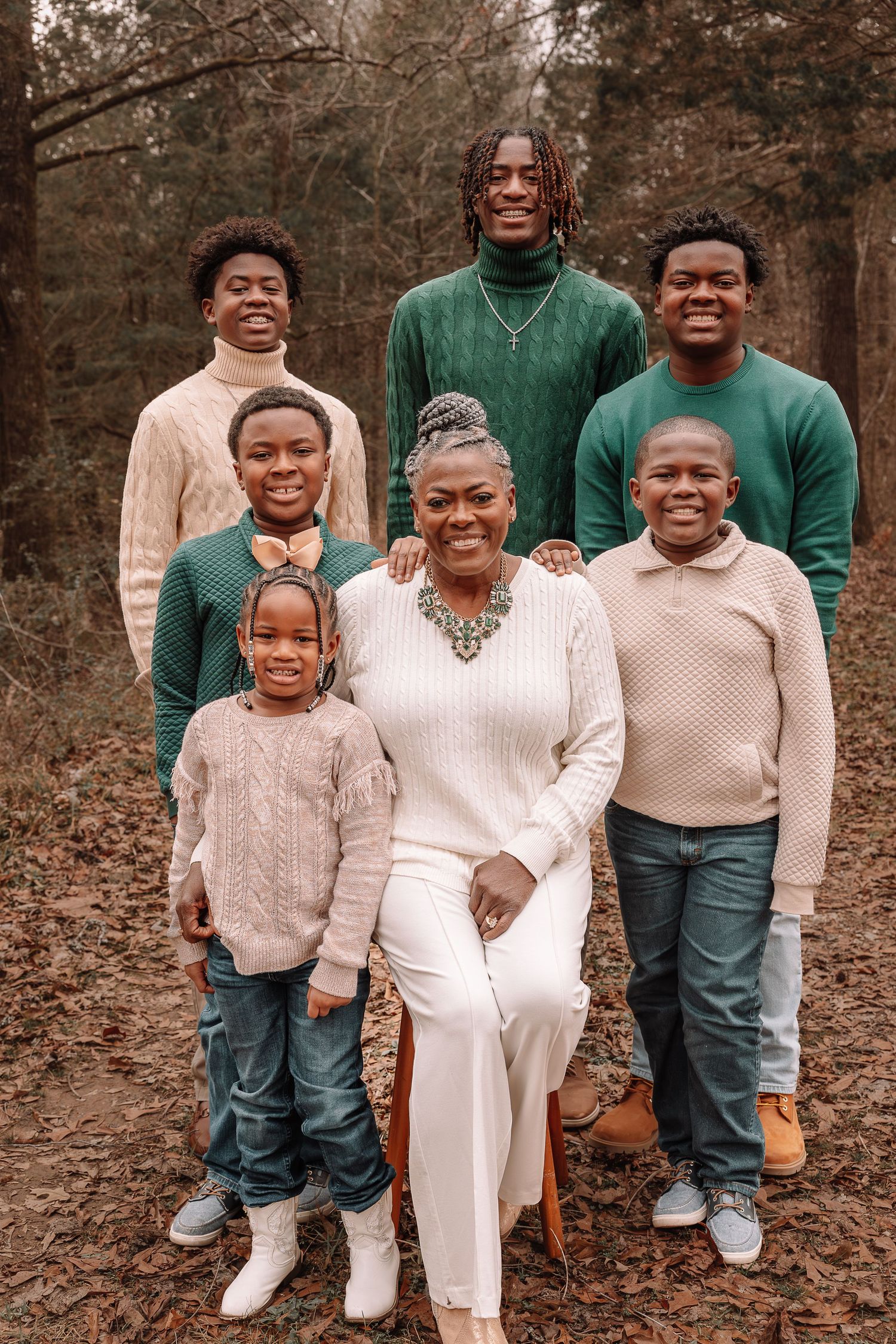 Family wearing coordinated green and beige outfits poses together outdoors among autumn trees.