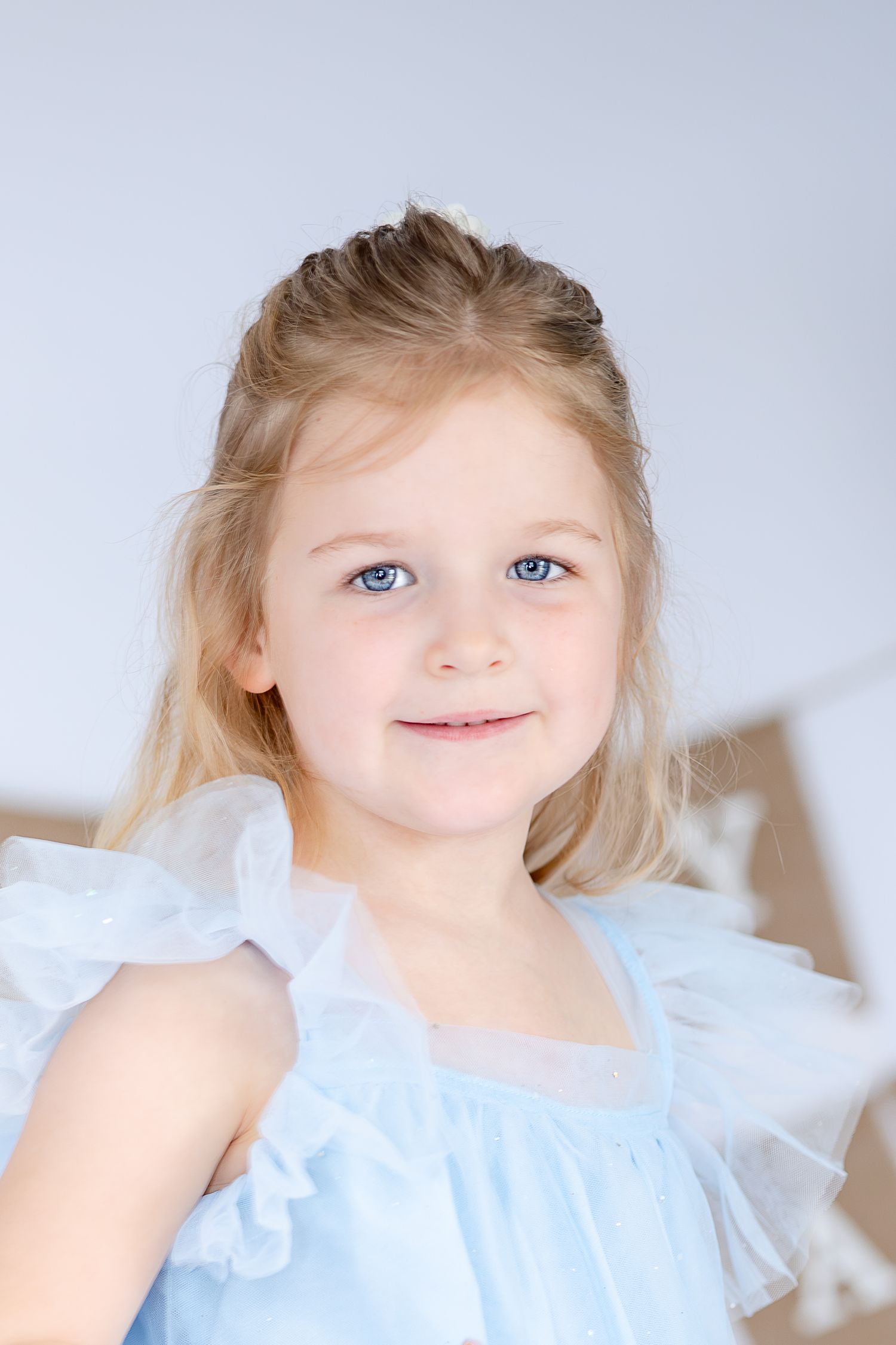 A child in a white ruffled dress smiles sweetly in a series of four ethereal portraits against a light background.