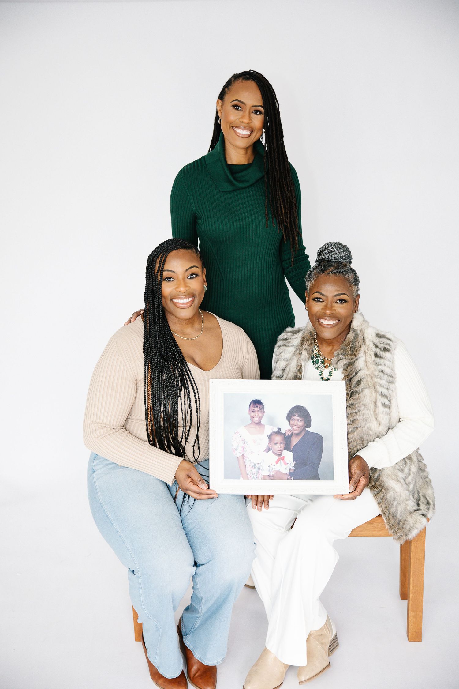 Three people pose together while holding a framed photograph against a white background.