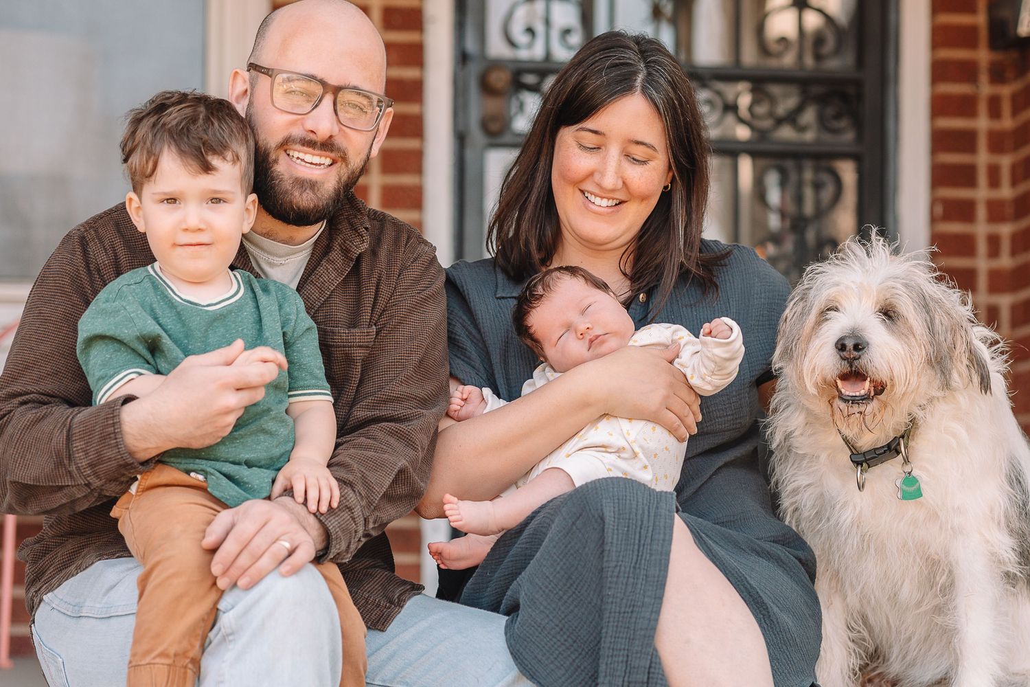 A family sits together outdoors with their white fluffy dog during a portrait photography session.