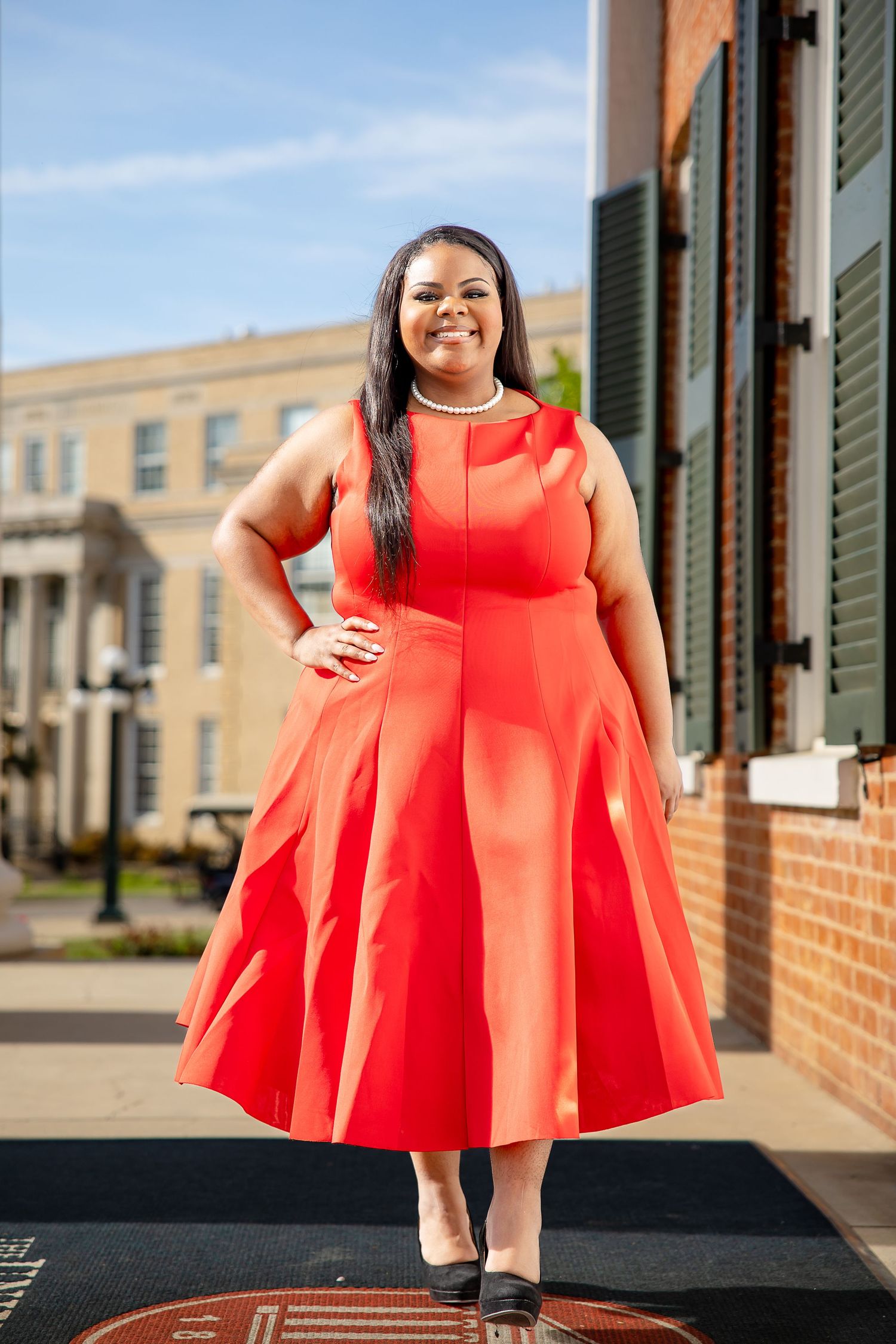 Woman in red midi dress posing outdoors on a brick sidewalk in front of a classic building.