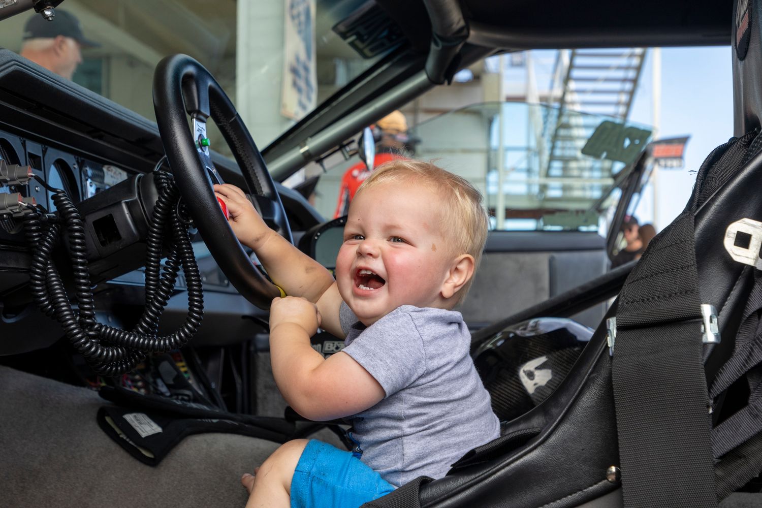 Smiling toddler behind the wheel in the pits at Rad Torque Raceway — future racer energy in full force.