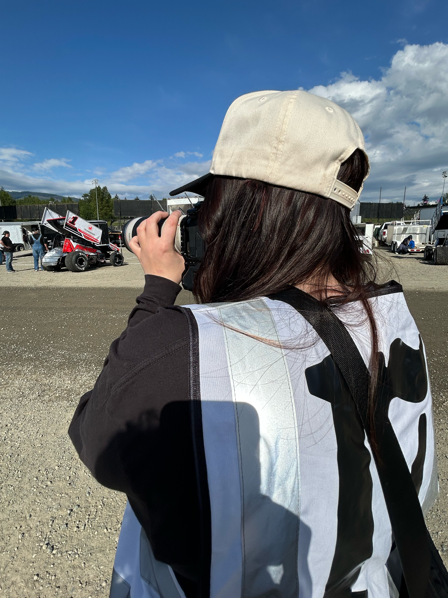 Becky from Fuelled Up Photography photographing trackside in a white cap and vest, camera up and ready to capture action.