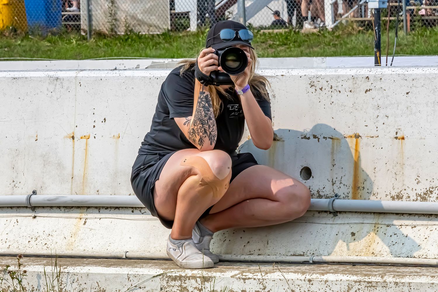 Becky crouched on pit wall with a camera mid-shot, repping Fuelled Up Photography at the track.