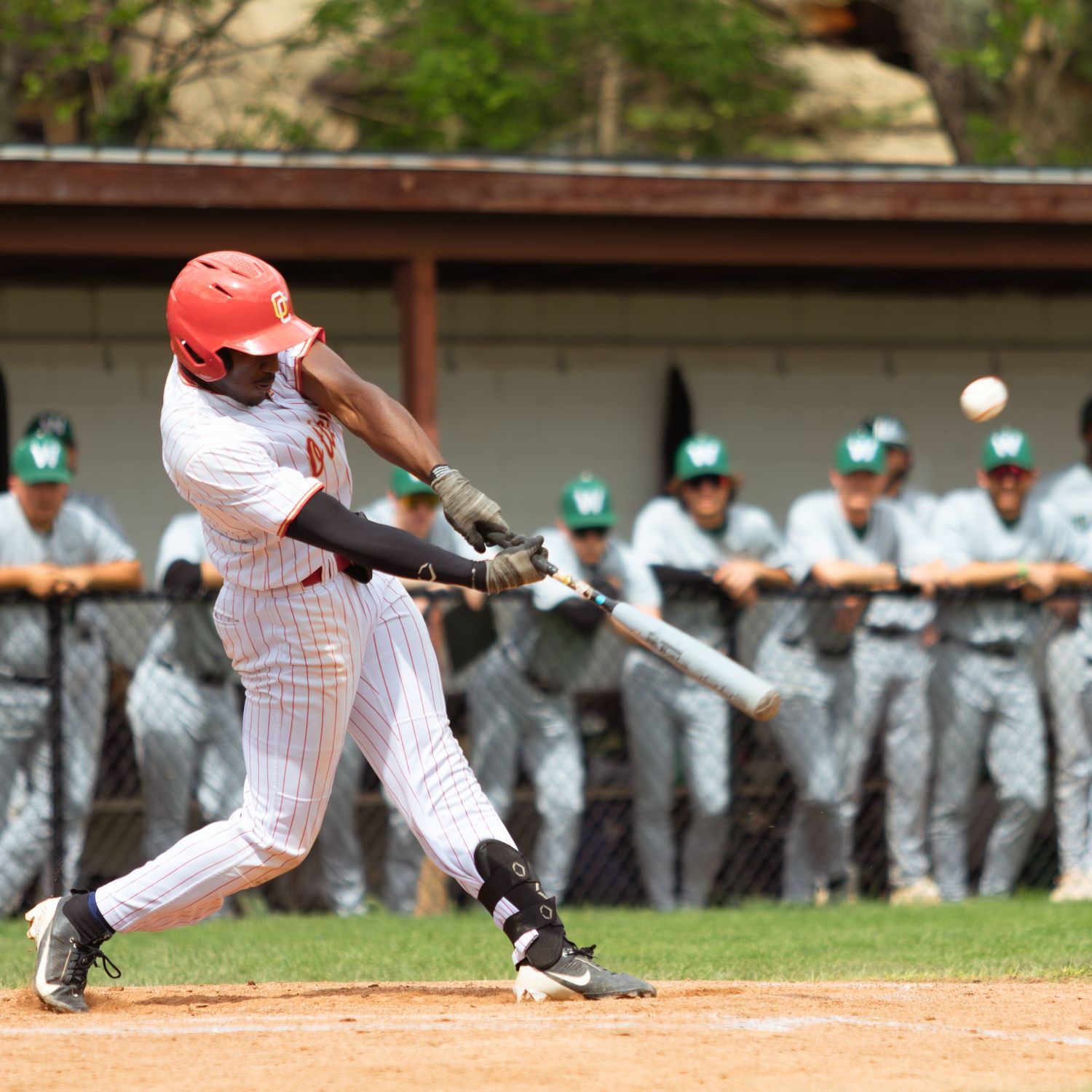 Baseball player in pinstripe uniform swinging bat during game with dugout in background.