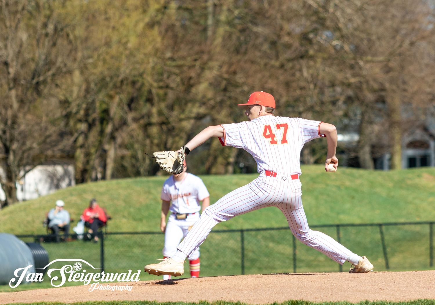 Baseball player in white uniform numbered 47 jumps off pitcher's mound during game action on sunny day at field.