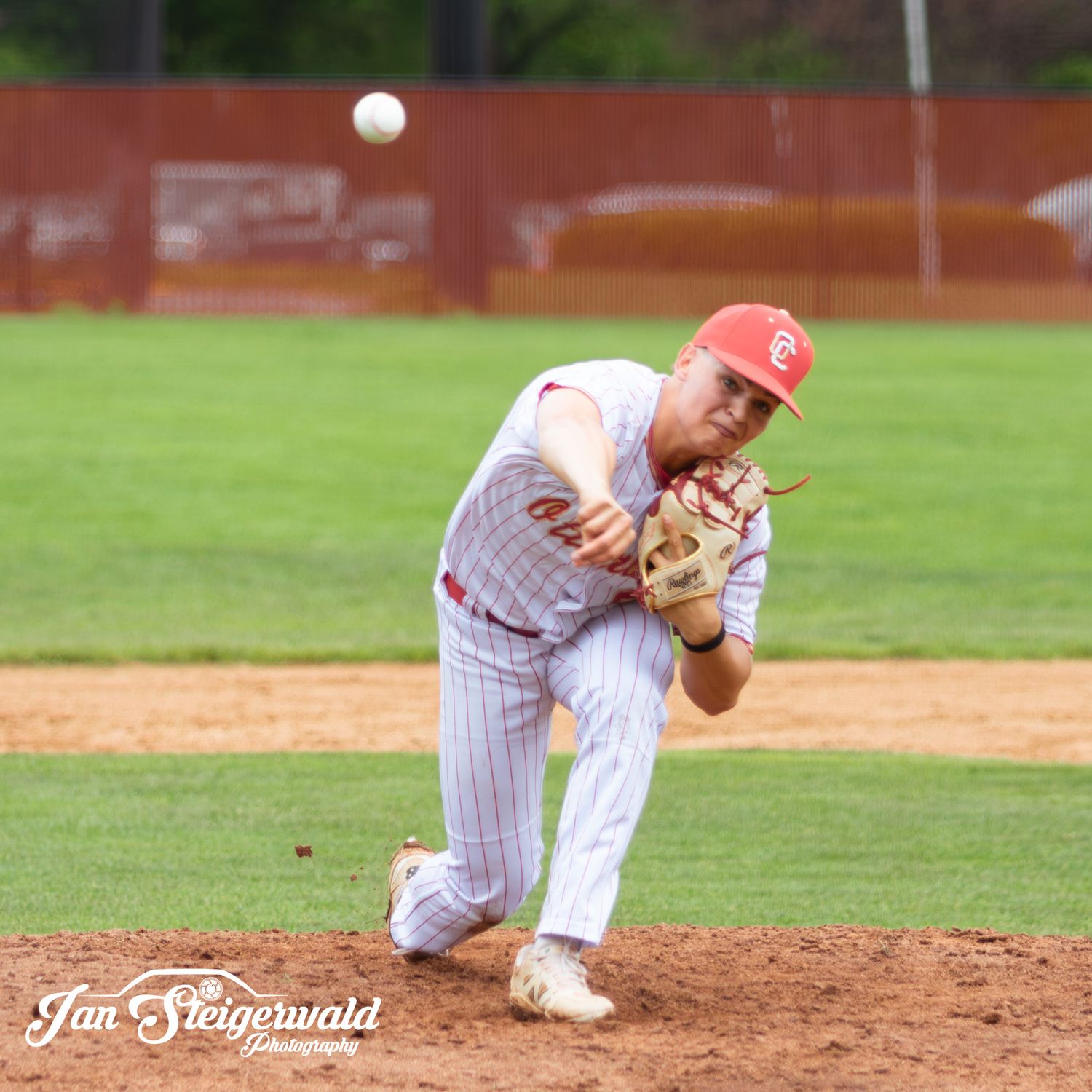 Baseball pitcher in pinstriped white uniform follows through on delivery during game on grass field.
