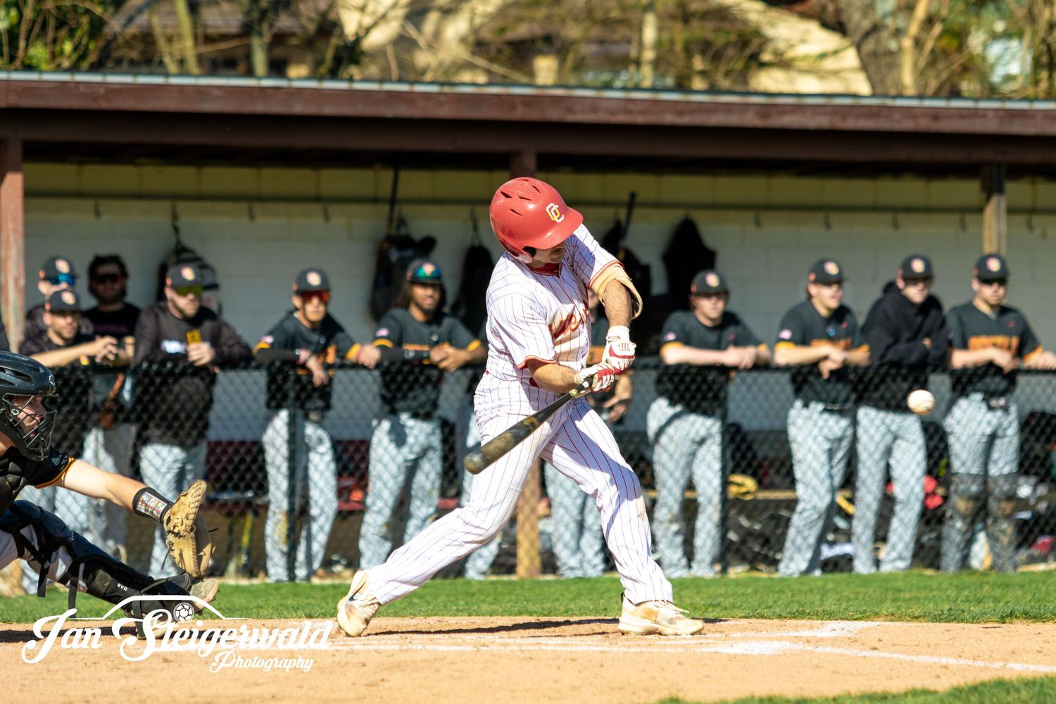 Baseball player performs a pitching motion during a game while teammates observe from the dugout area.