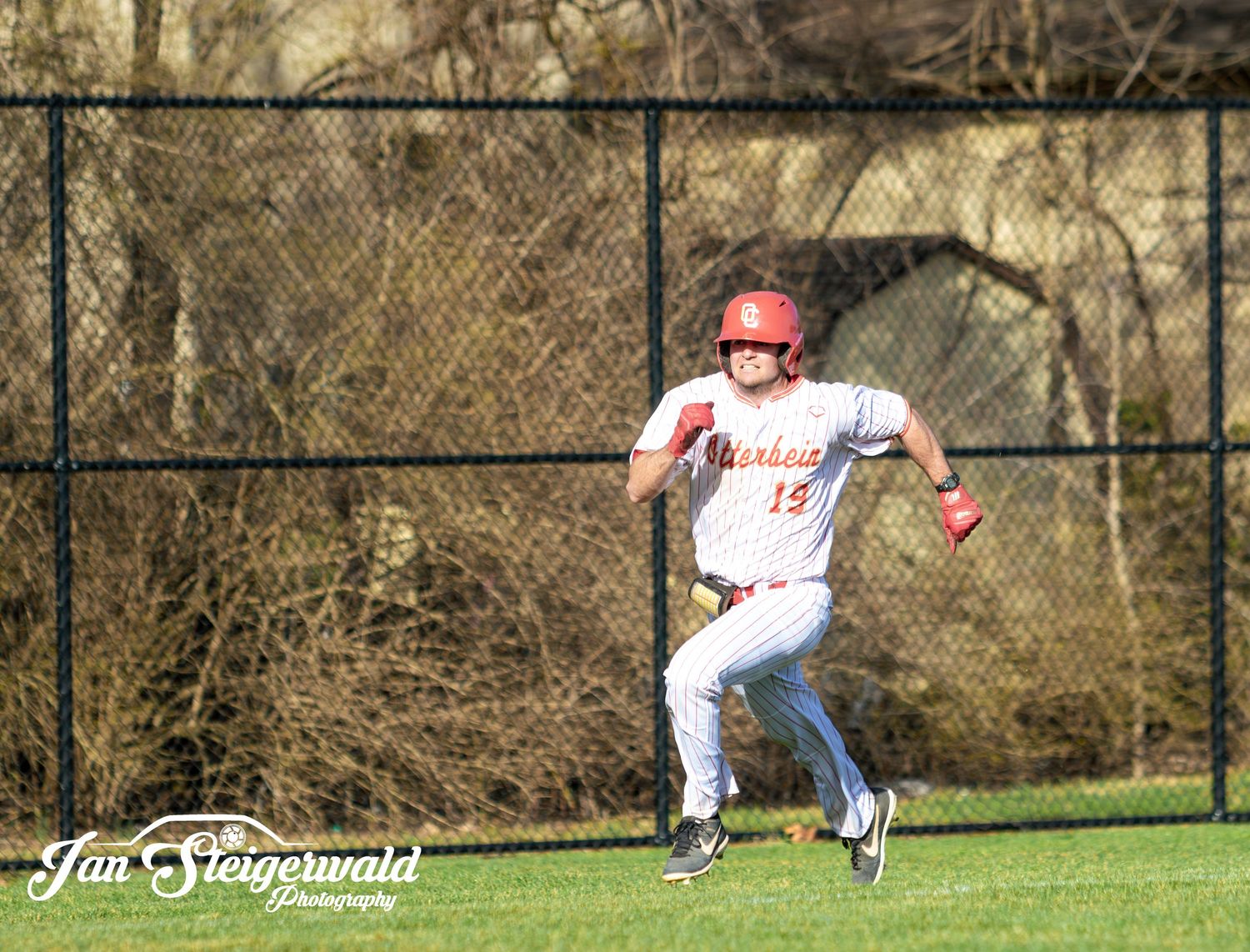 Baseball outfielder in white uniform and red cap sprints across the grass field during gameplay.