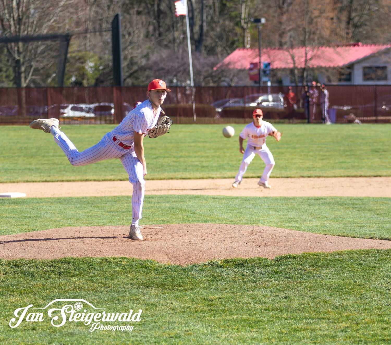 Baseball pitcher in white uniform follows through on delivery from the mound during a game on sunny day.