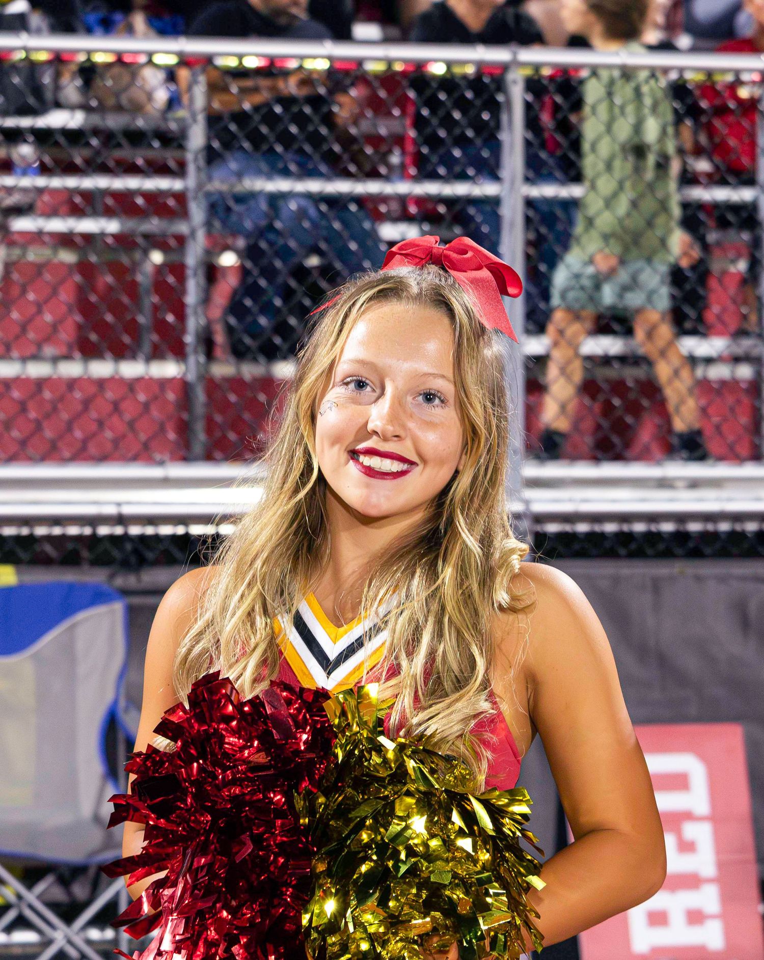 Cheerleader in red and white uniform holding pom poms at football game.