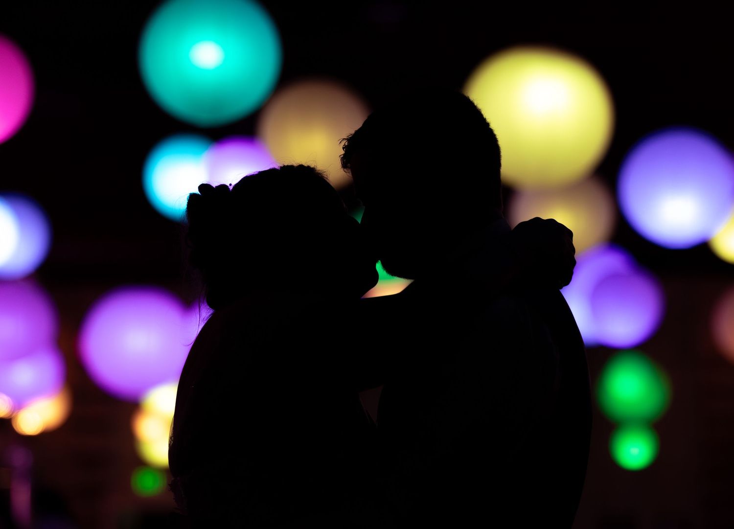 Silhouetted figures against a backdrop of multicolored glowing orbs at night.