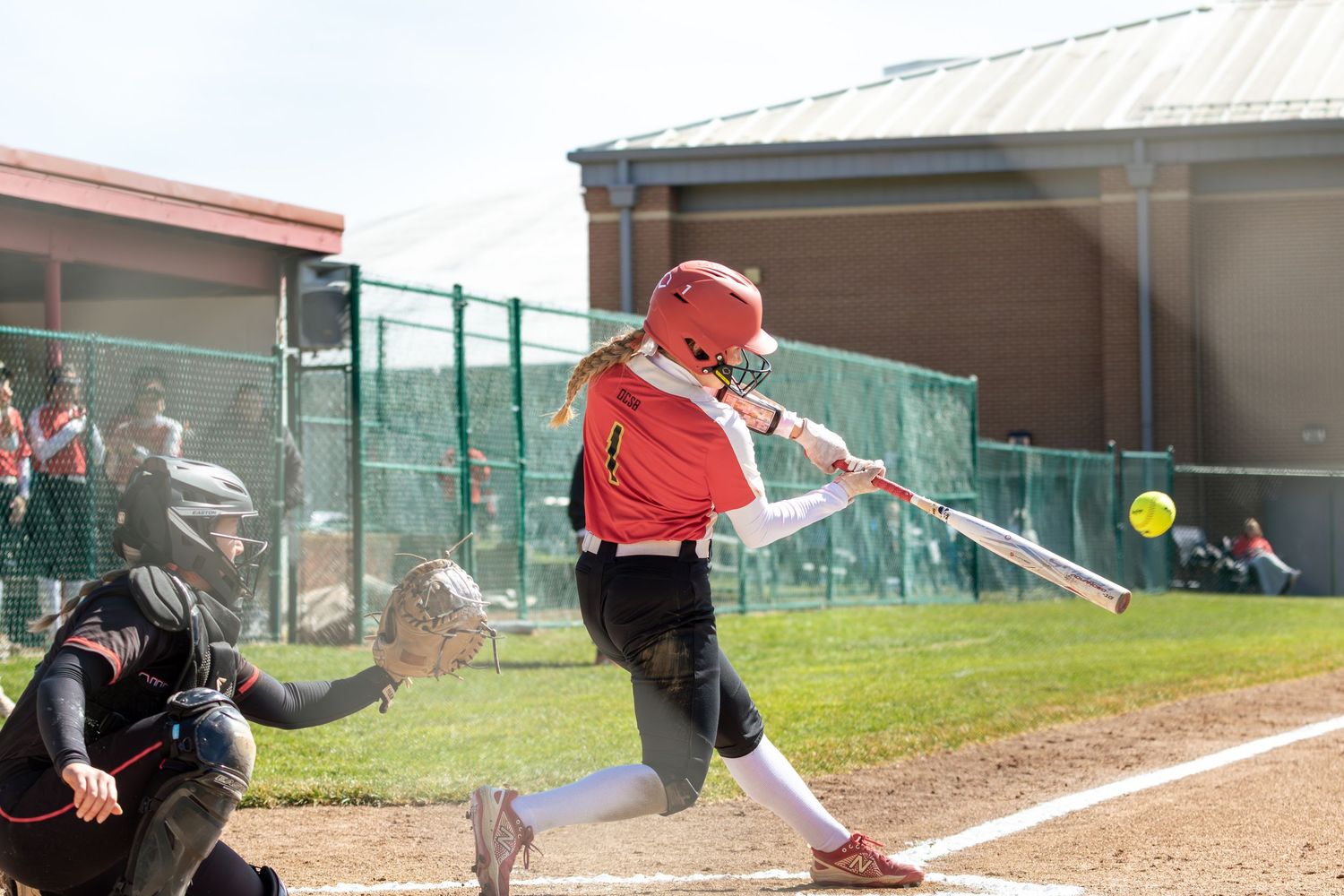Softball player in red uniform swinging bat at yellow ball during game.